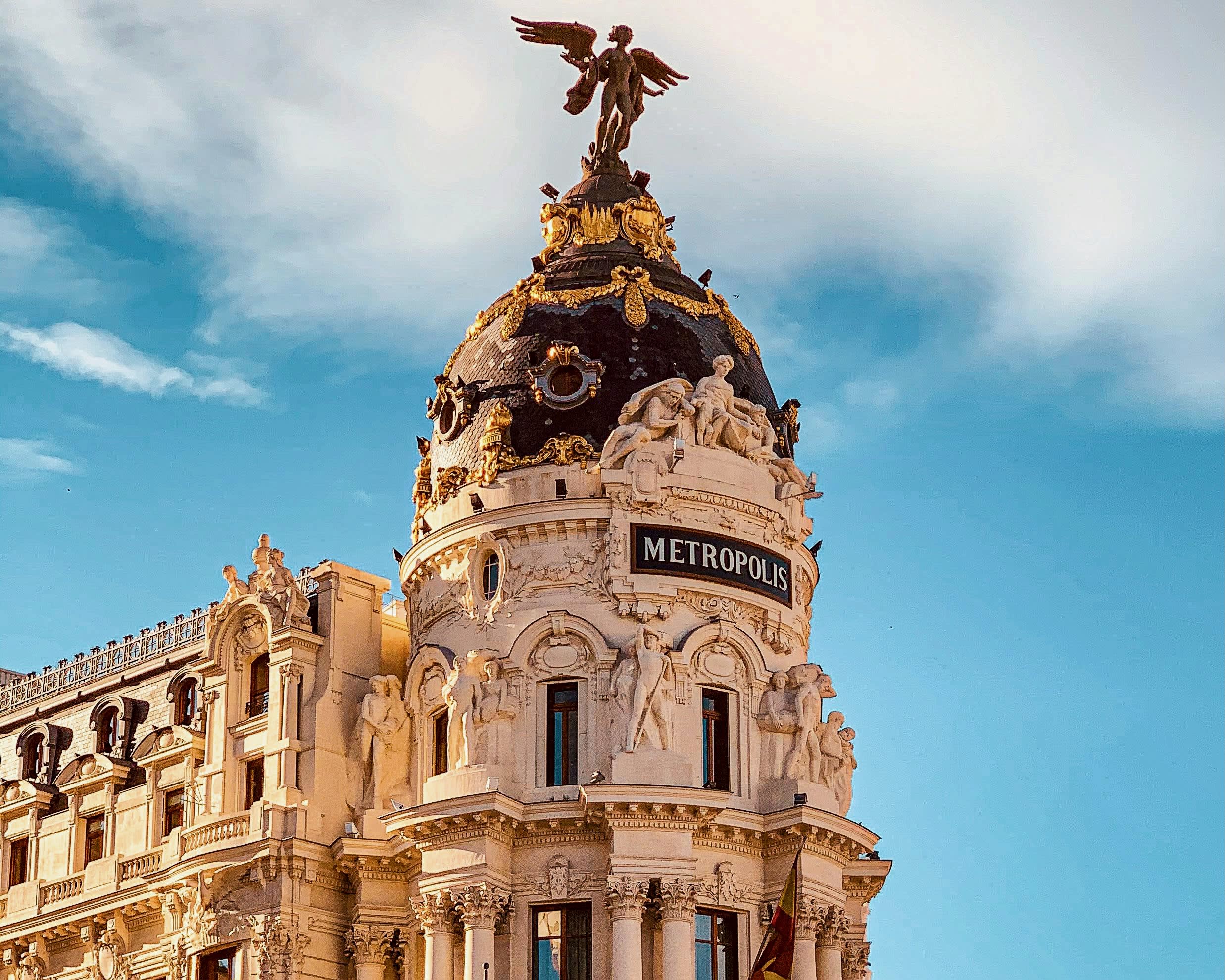 tall ornate building facade with black and gold domed roof with angel figure on top 