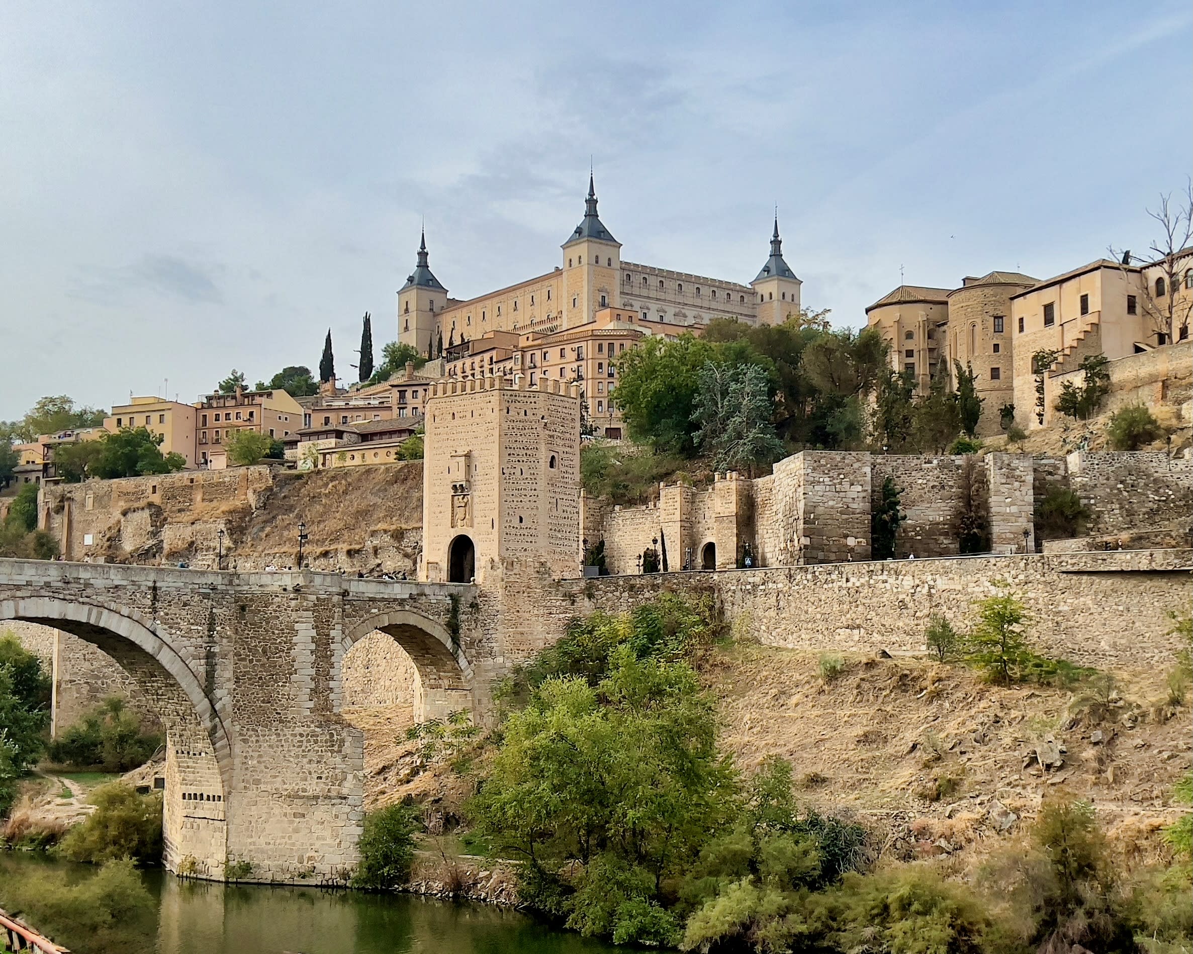 stone bridge over a river leading to a stone hilly town with fort at the top