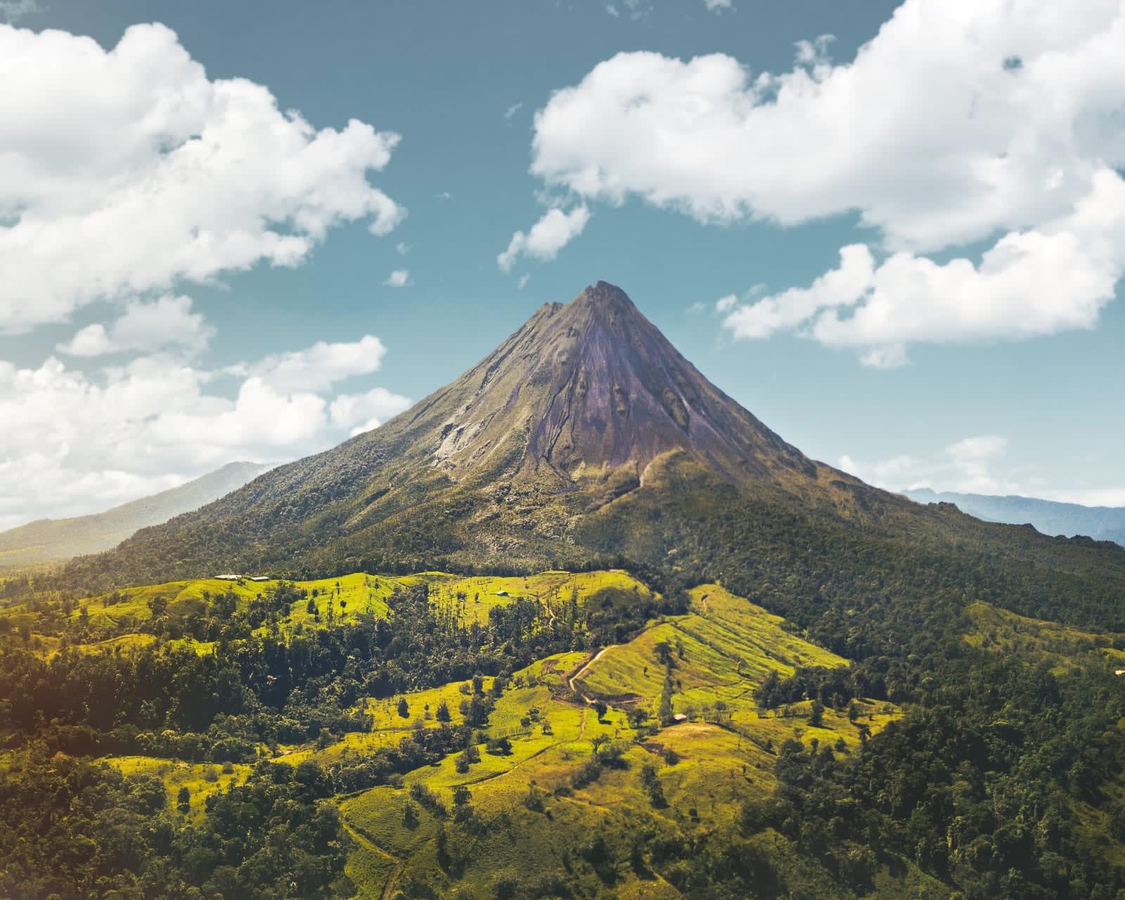 volcano rising above green valleys into blue skies with white clouds