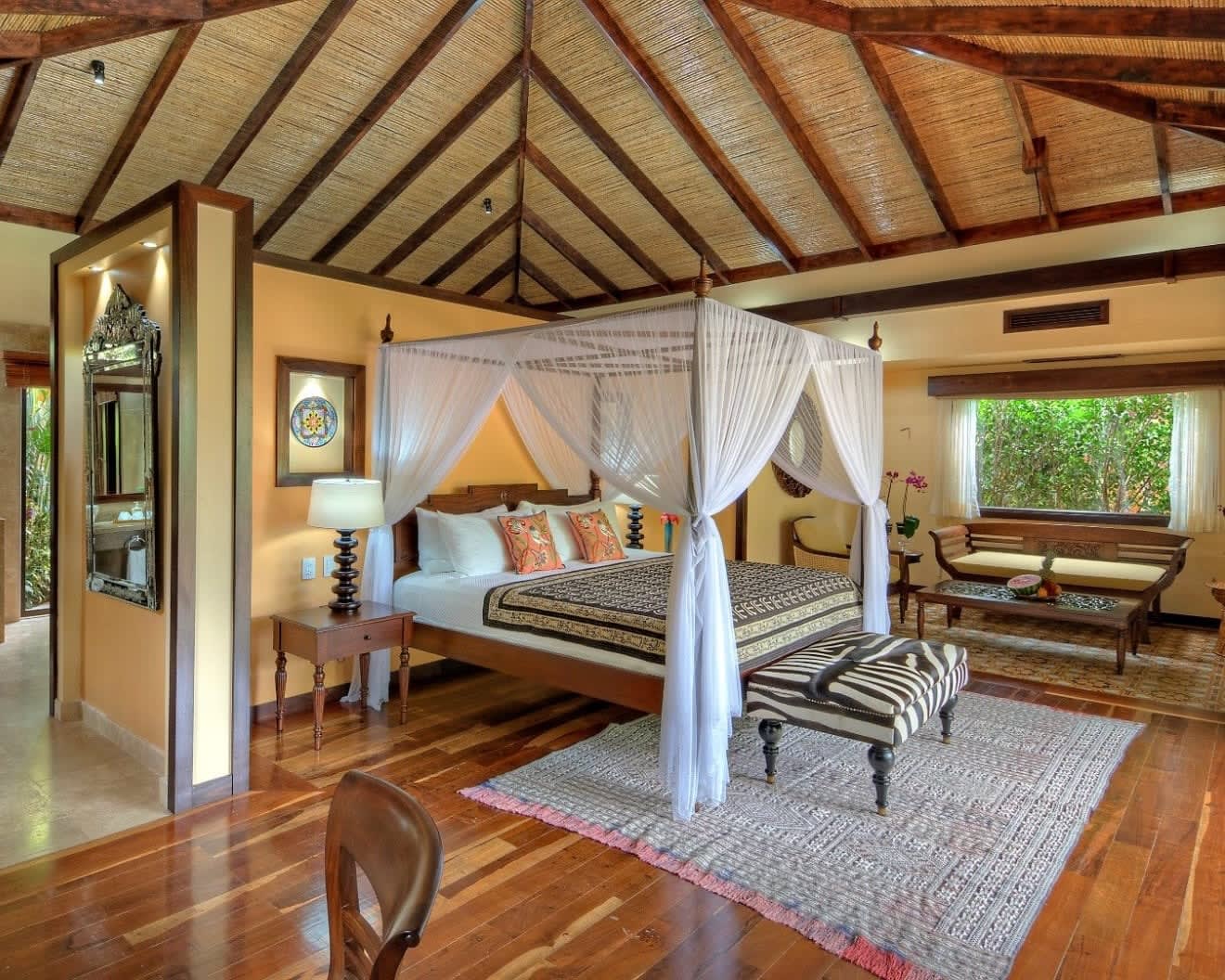 four poster bed with white curtains under a thatch roof bungalow roof