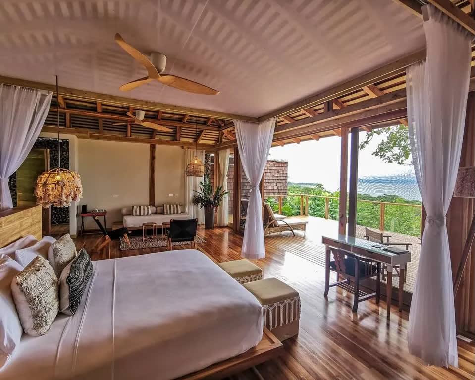 bed under a canopy of curtains opening out onto a balcony with tree top views