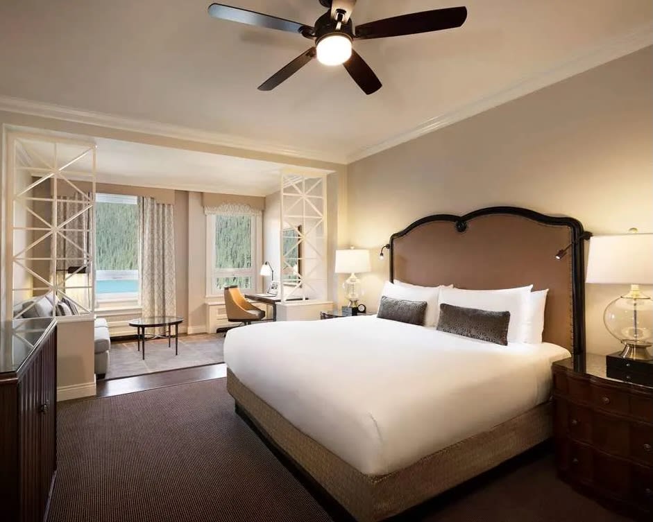 hotel room with white bed, brown headboard, and seating area next to windows overlooking wilderness