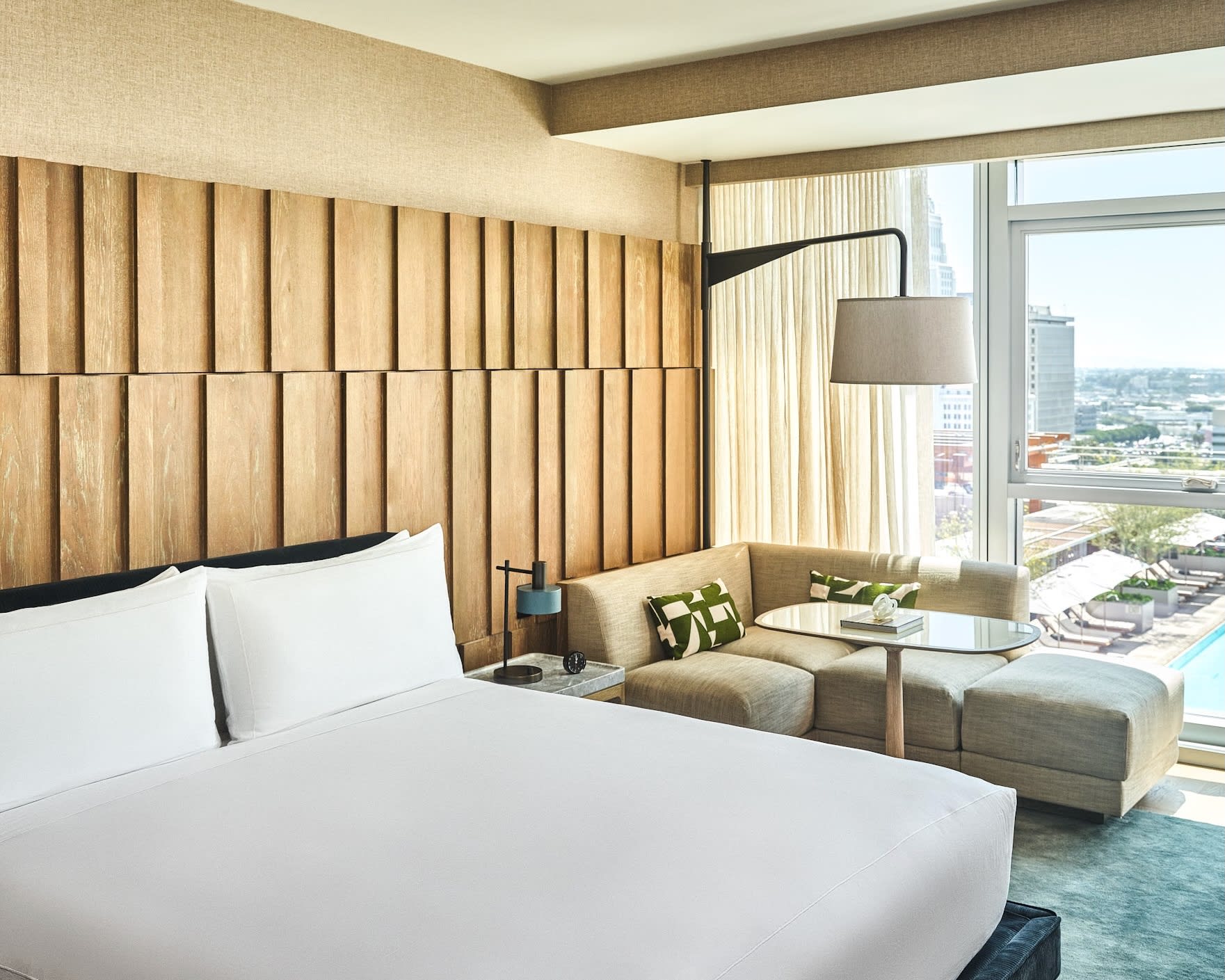 white hotel bed next to tan chaise lounge, and a wood textured wall behind