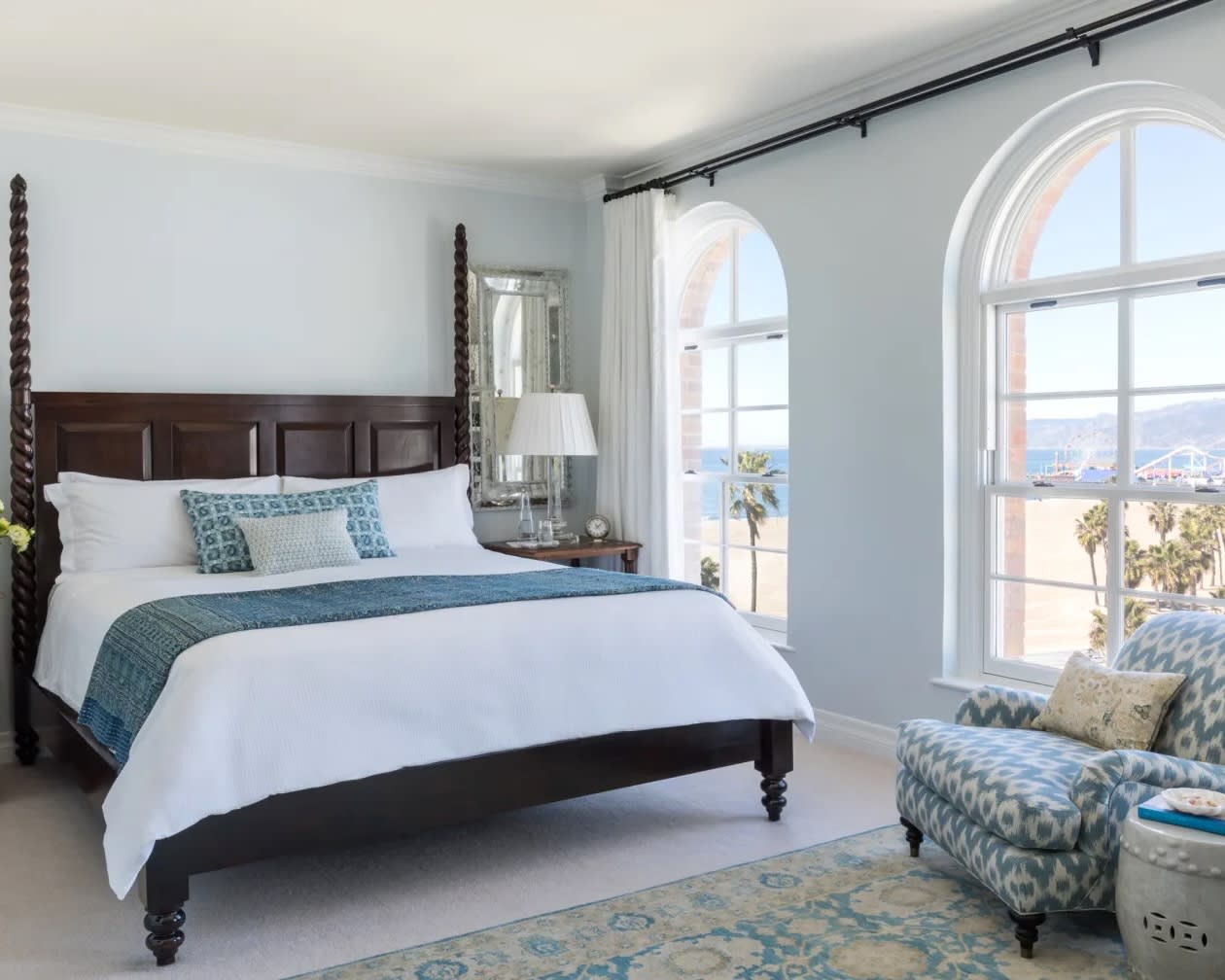 dark wood four poster bed with white sheets, light blue accent decor, and windows looking onto the beach