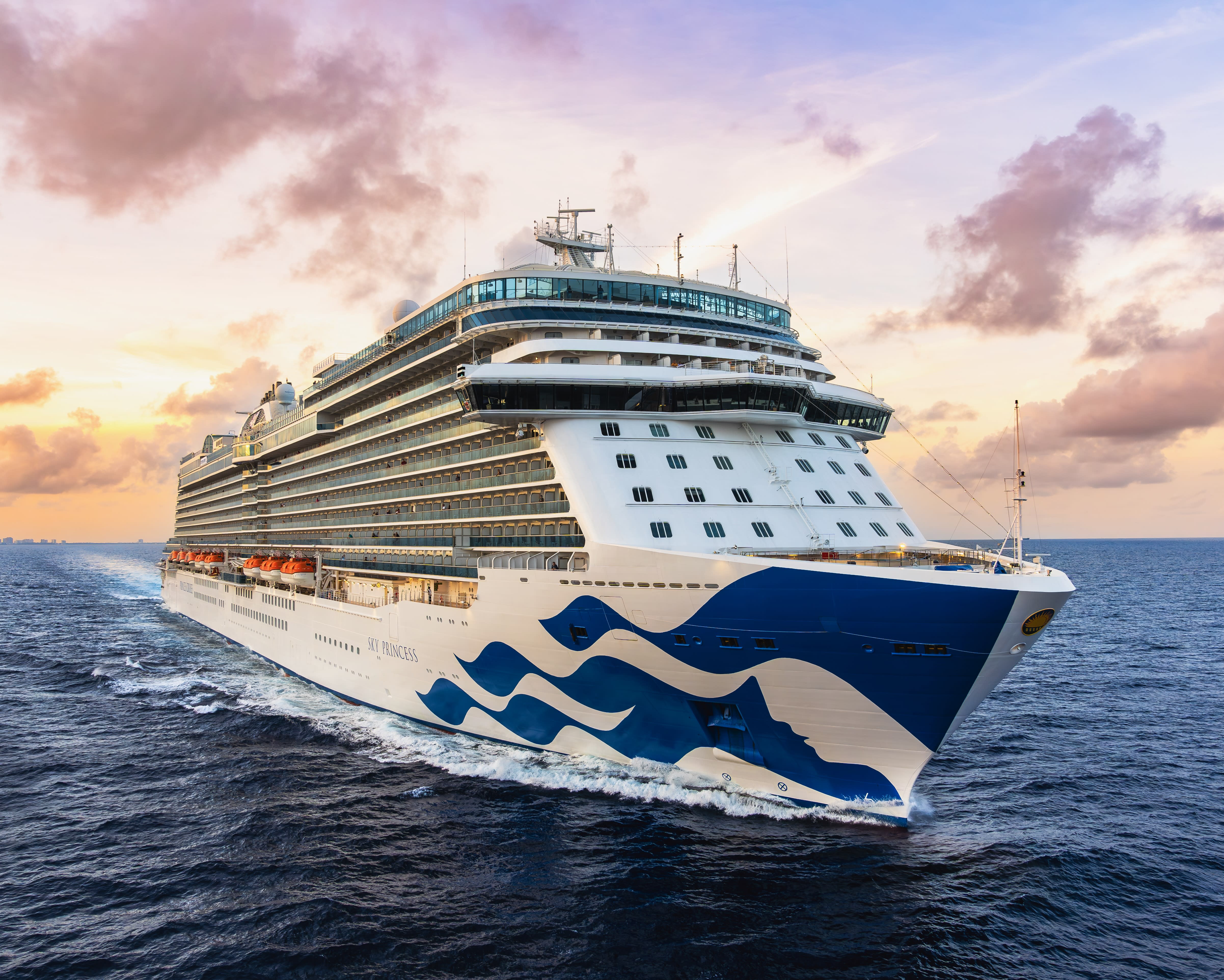 large white and blue cruise ship sailing through blue ocean waters at sunset