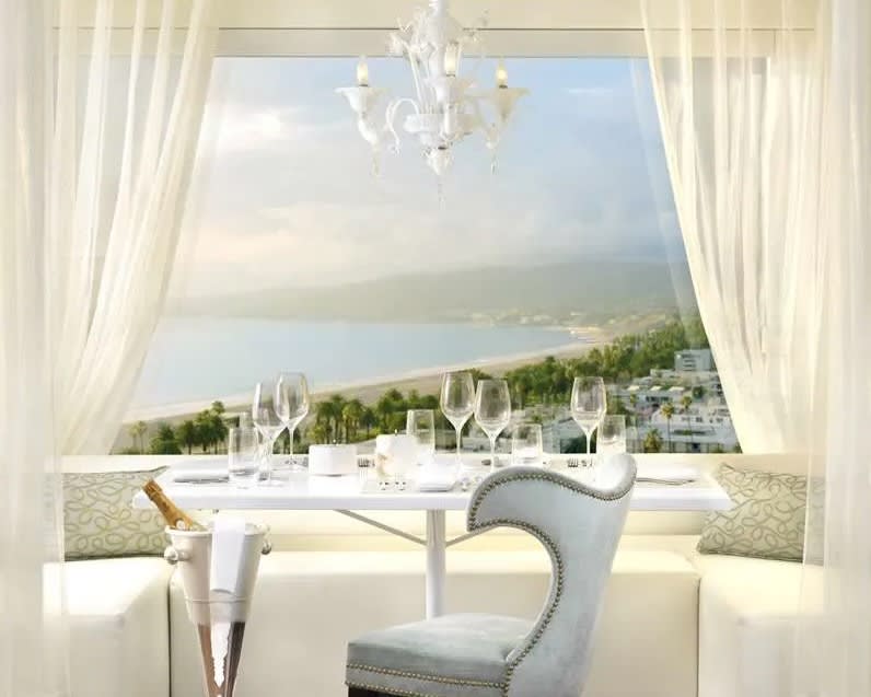 white dinner tables and chairs overlooking an aerial coastal view