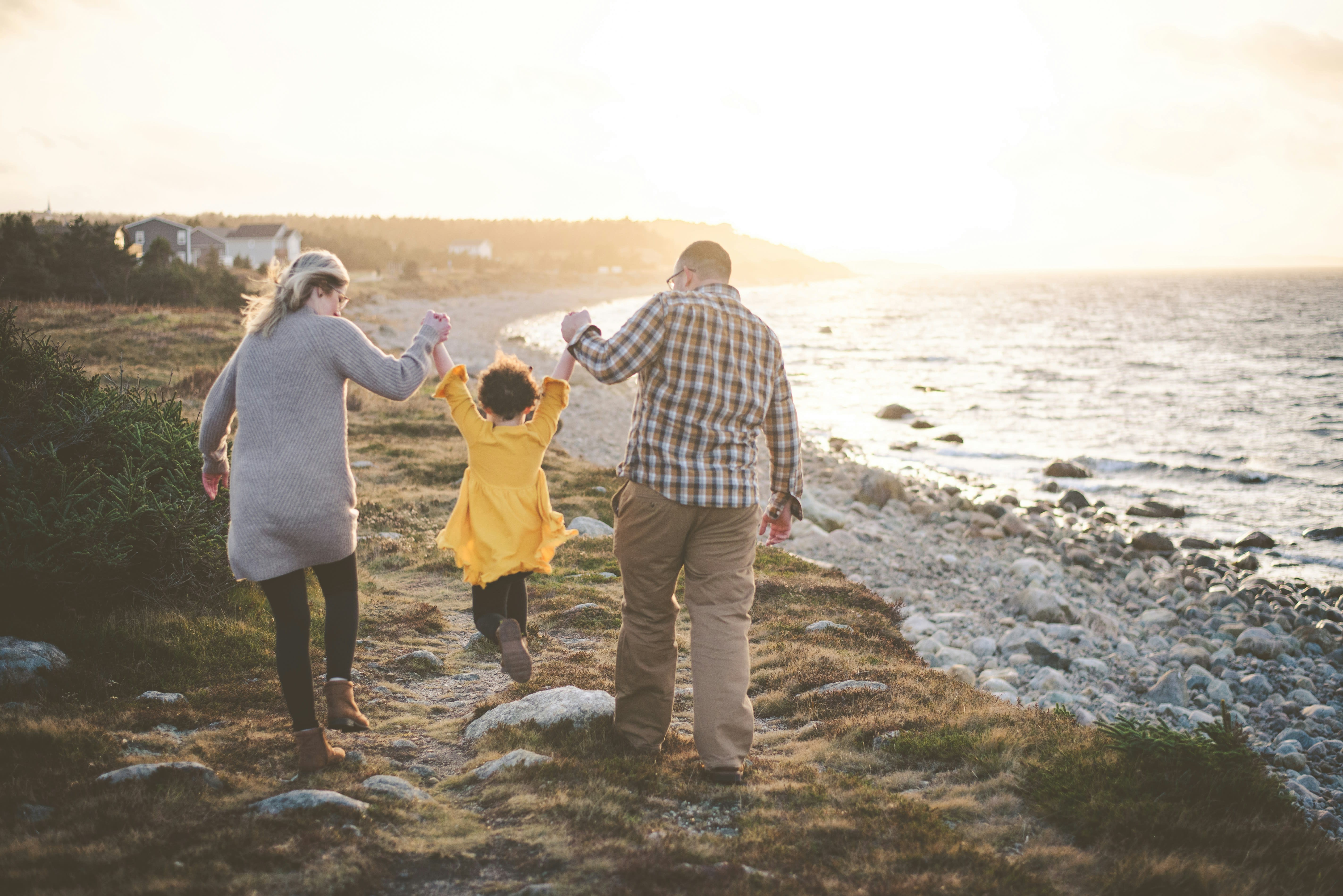 Two older individuals walk along a rocky beach at sunset with a small child