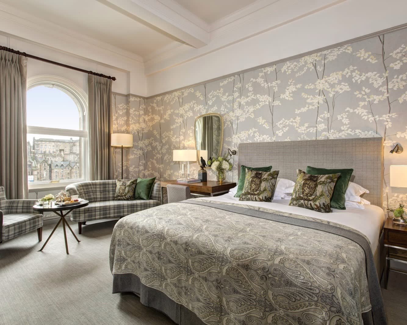 traditional hotel room with grey patterned bed and wallpaper, green tartan seating, and curtains