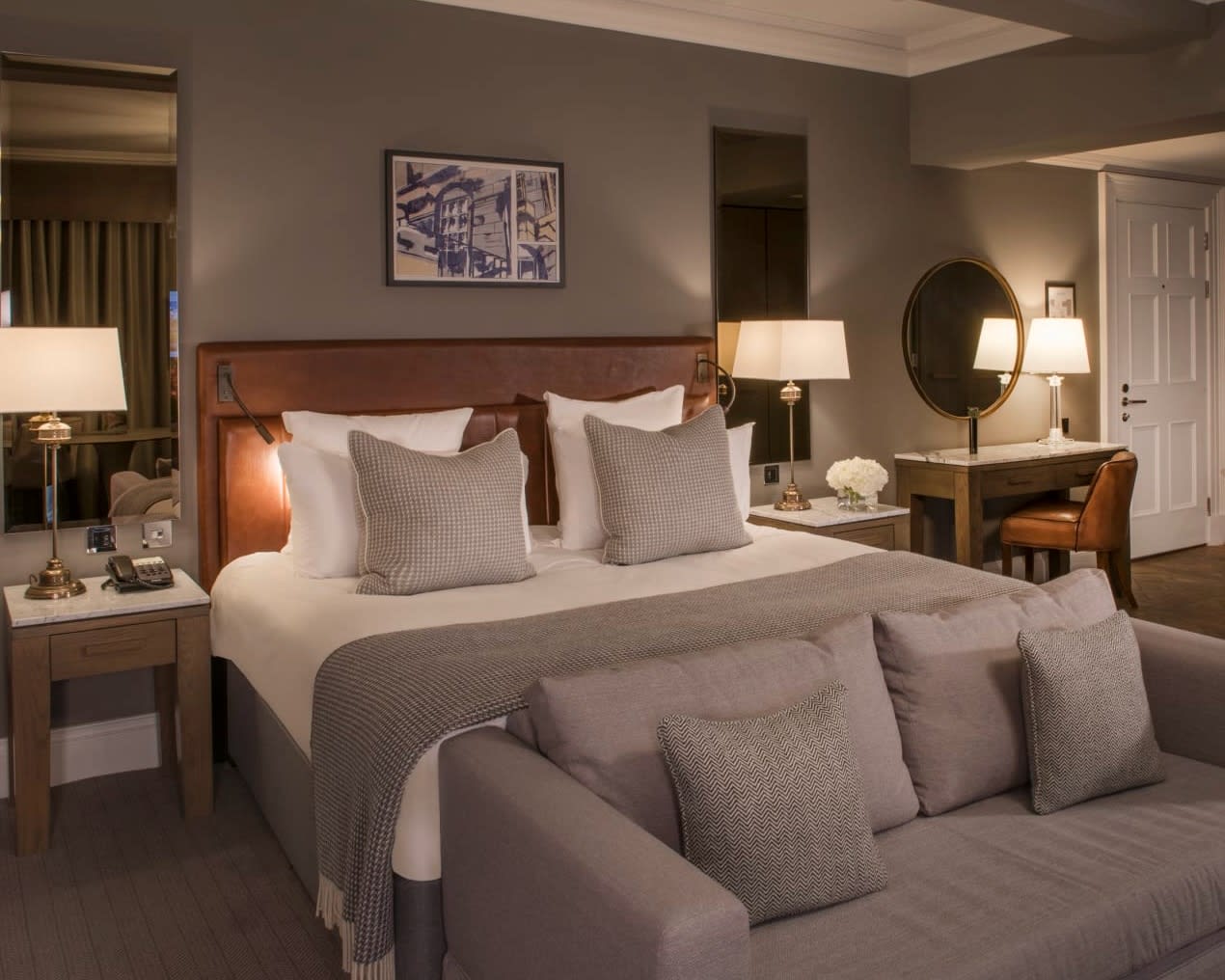 grey loveseat at the foot of a bed with grey accents, wood headboard, and tan walls