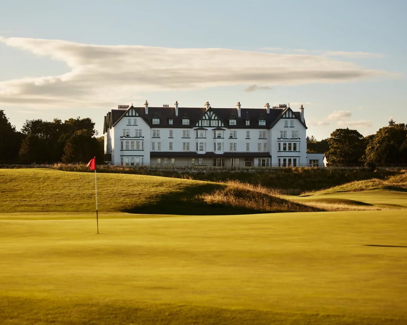 a green golf course hole with white estate house in the background during day