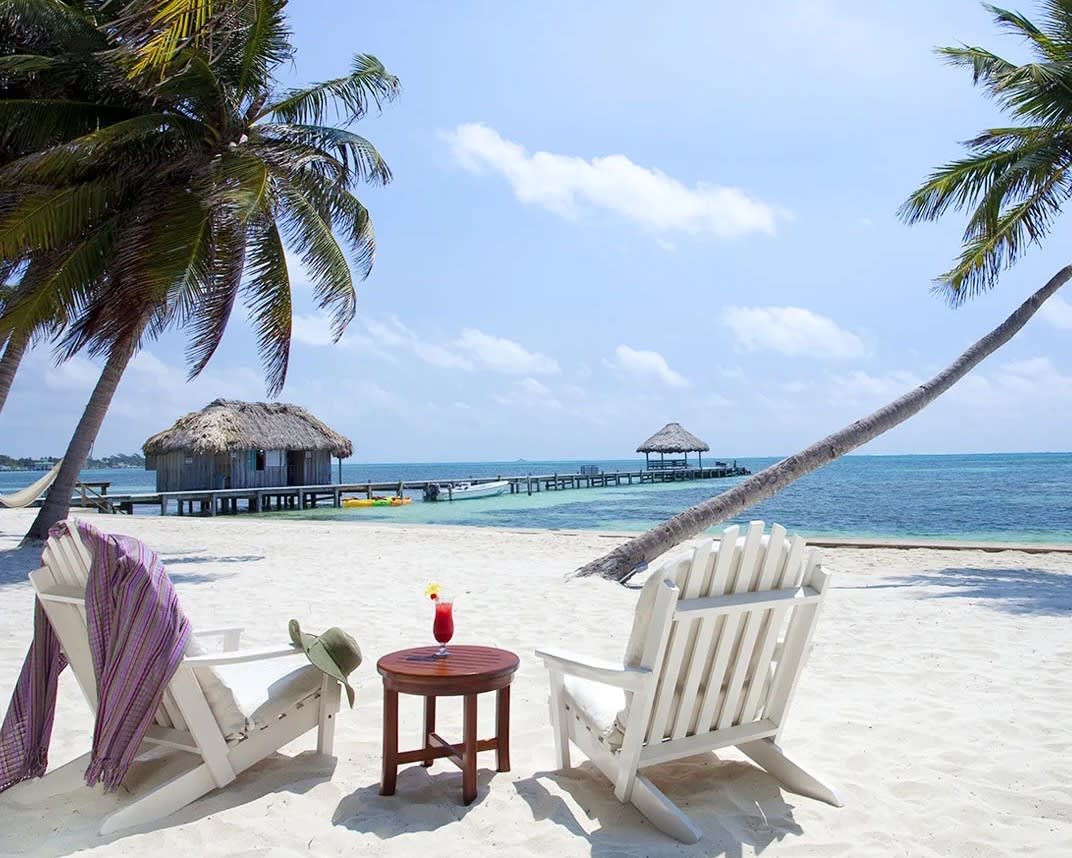 white beach chairs on a white sand beach with palm trees overlooking a blue ocean