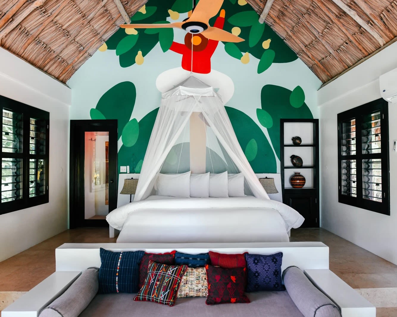 a white bed with mosquito net in front of a colorful painted wall and curved vaulted ceiling