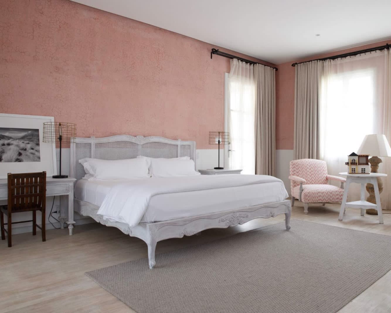 rustic hotel room with pink walls, white bed, and cream carpets