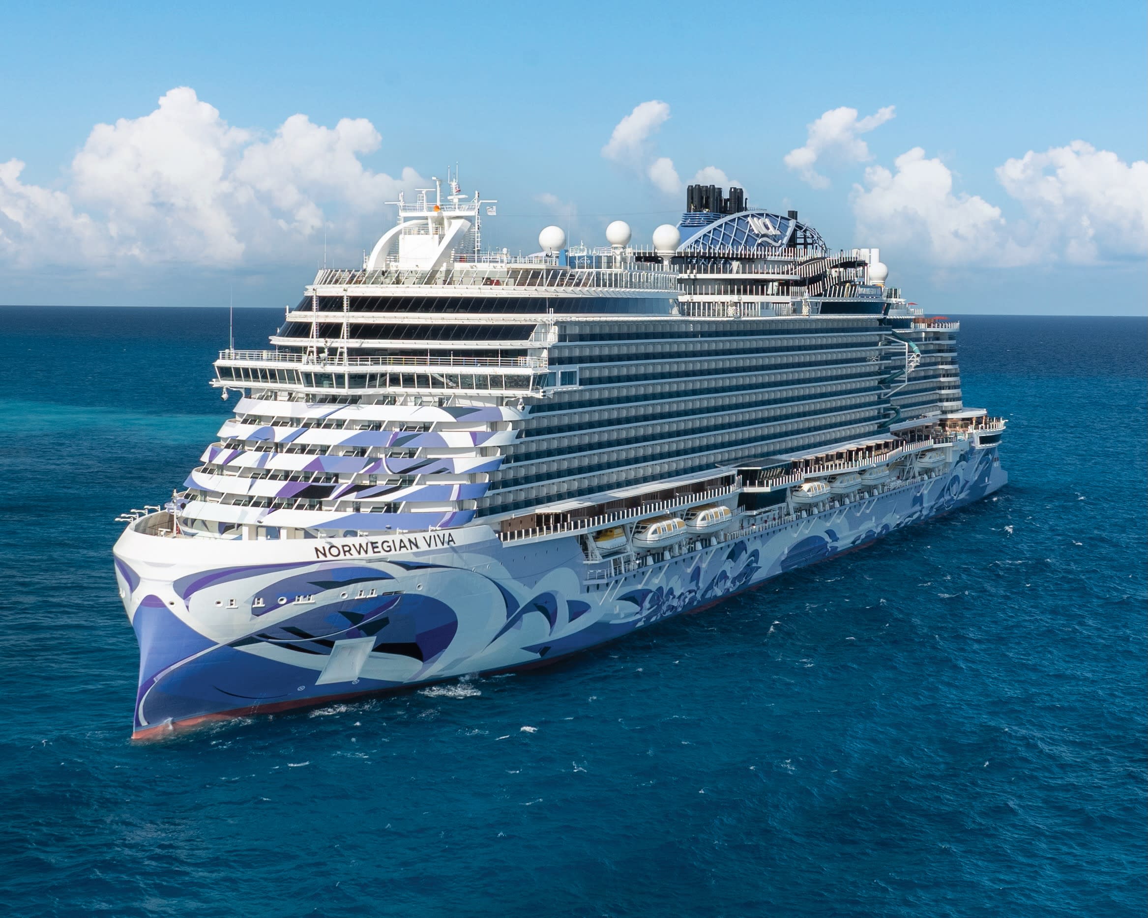 white cruise ship with purple painted hull art sailing on a turquoise ocean