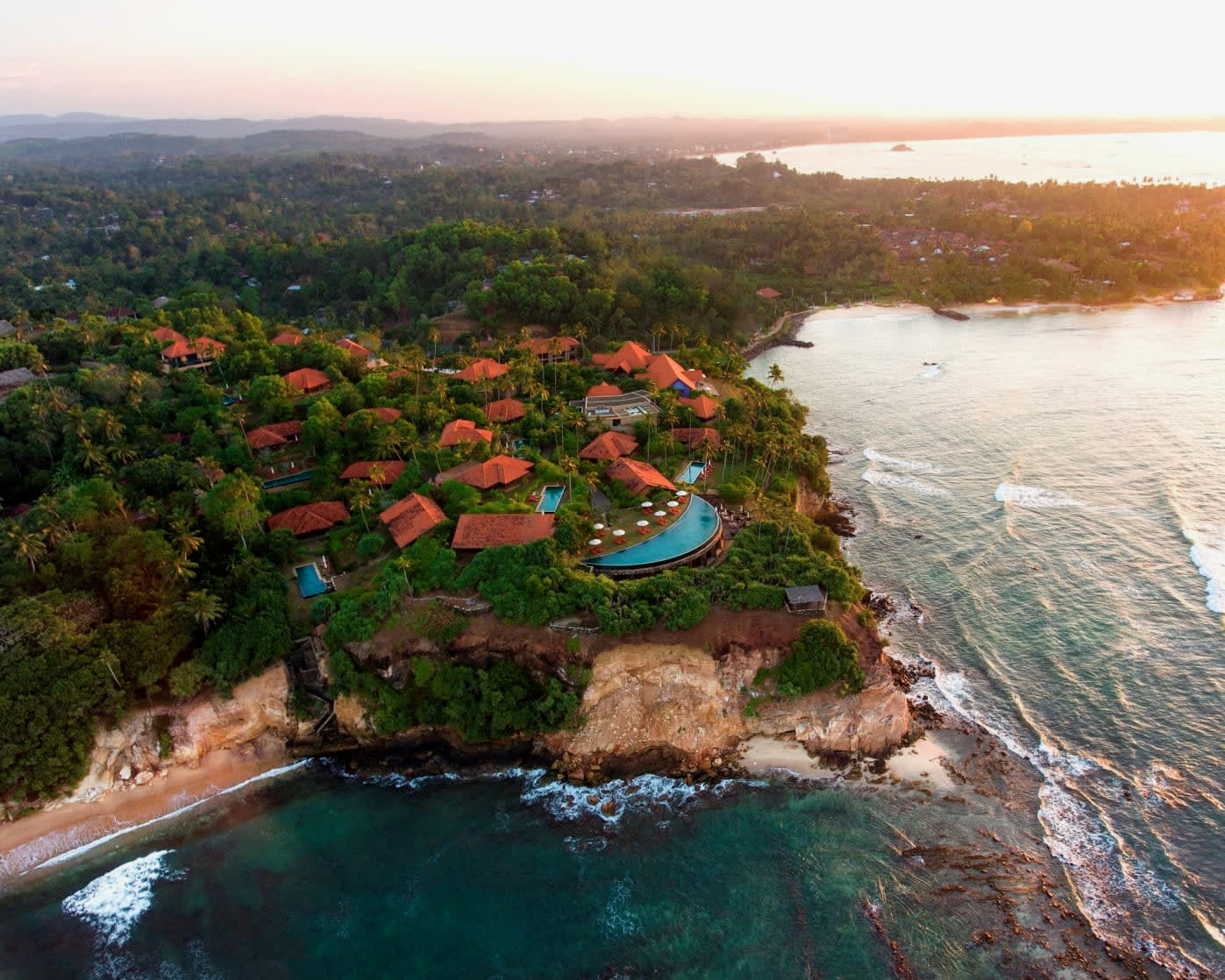 Aerial view of a clifftop luxury resort in the jungle with the sun setting over the ocean