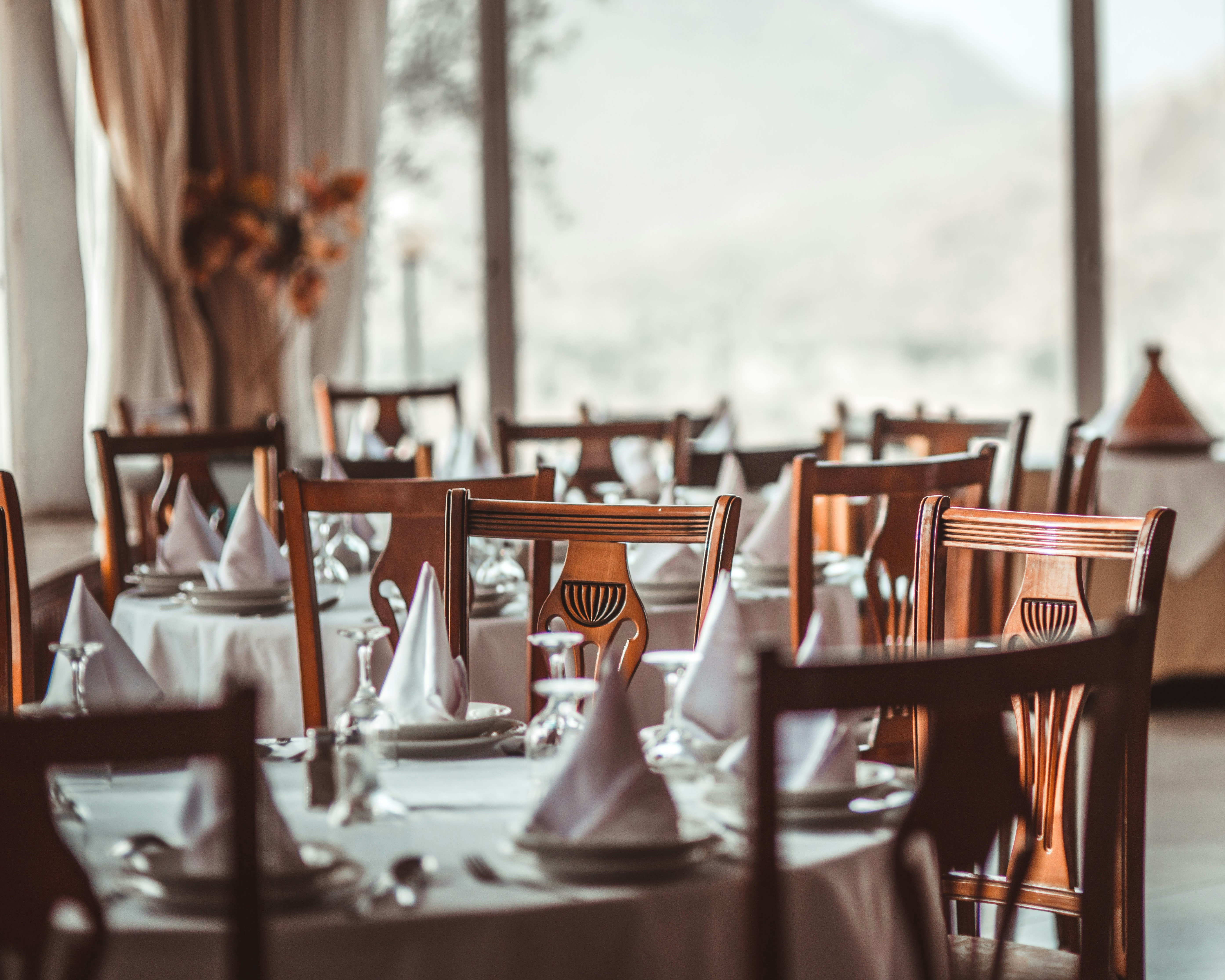 a restaurant with wood chairs around white tablecloth covered tables during day