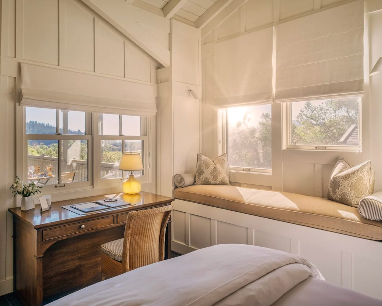 white cottage room with window bench and desk, and sun rising outside