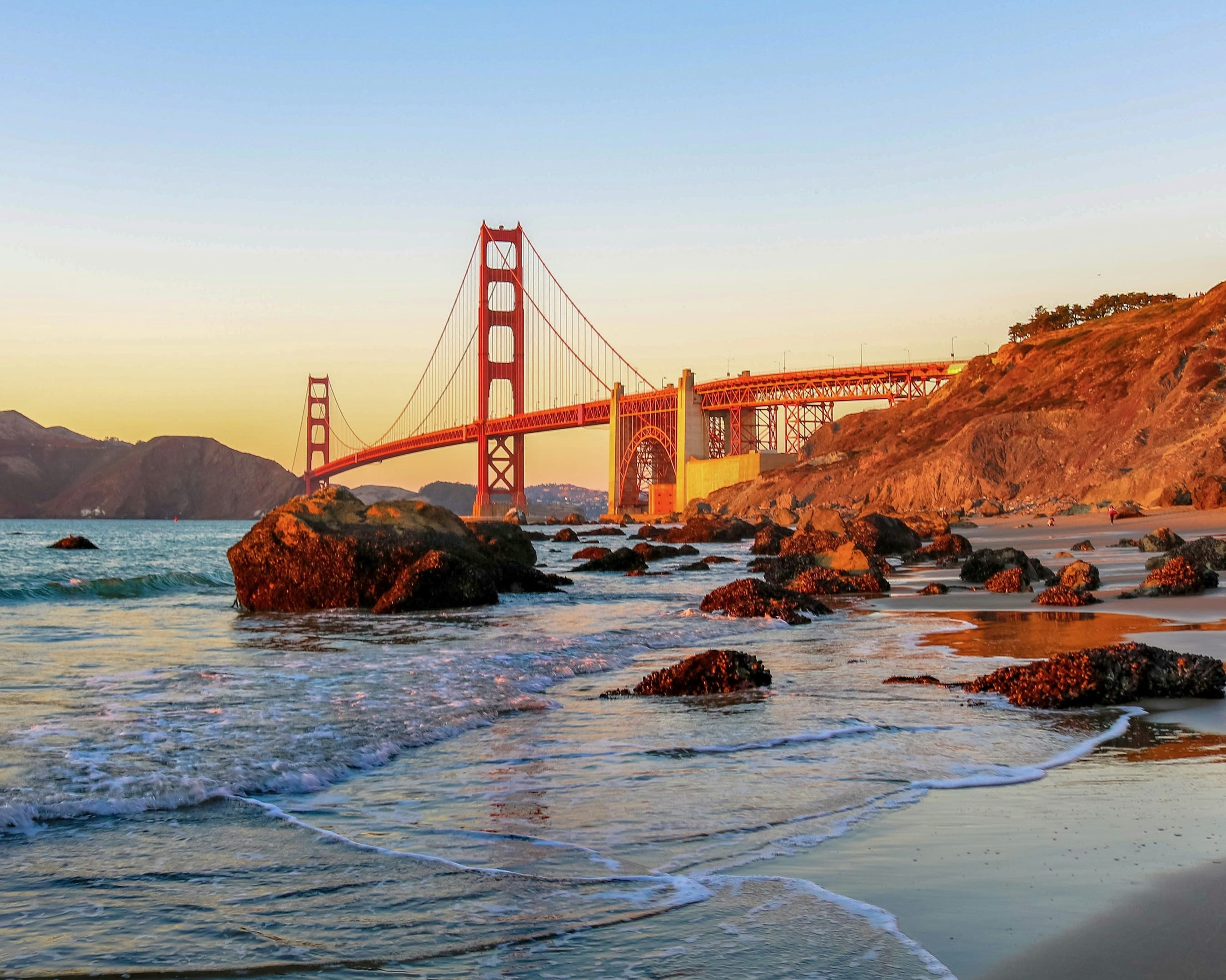 the sun setting with the red golden gate bridge over the water with mountains in the background