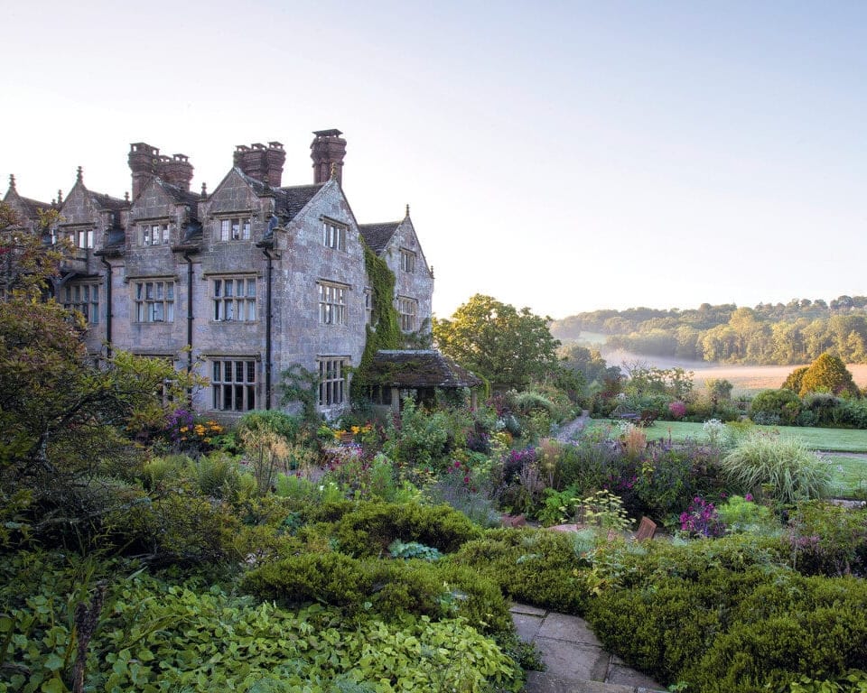 a rustic countryside manor house surrounded by colorful flowers and green shrubs
