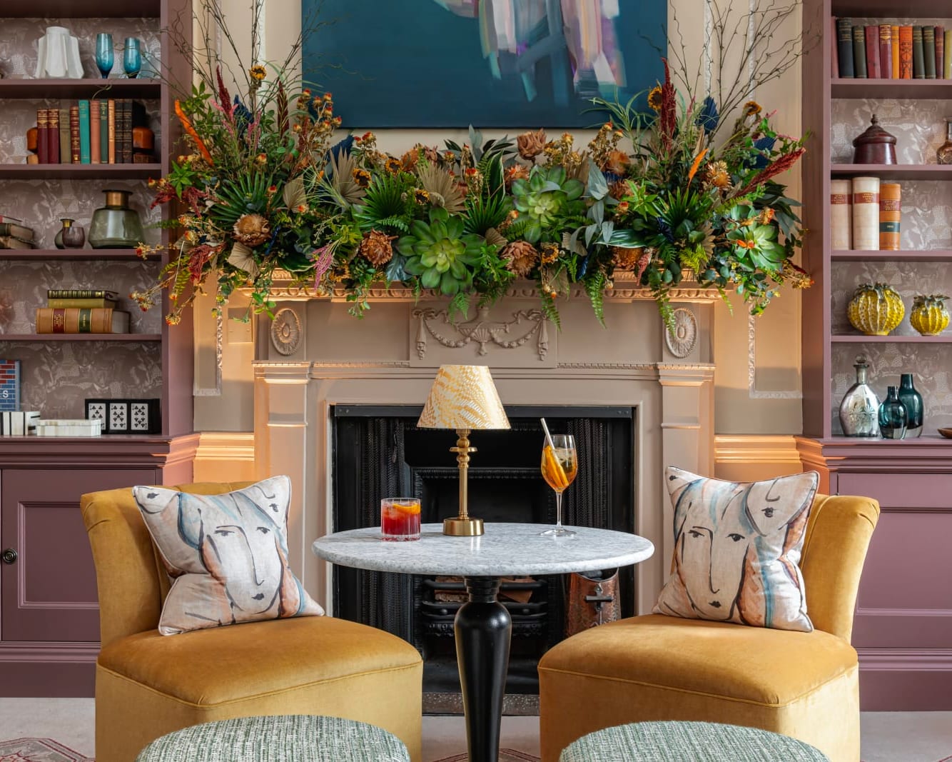 two yellow chairs with a white marble table in between, in front of a fireplace and book shelves