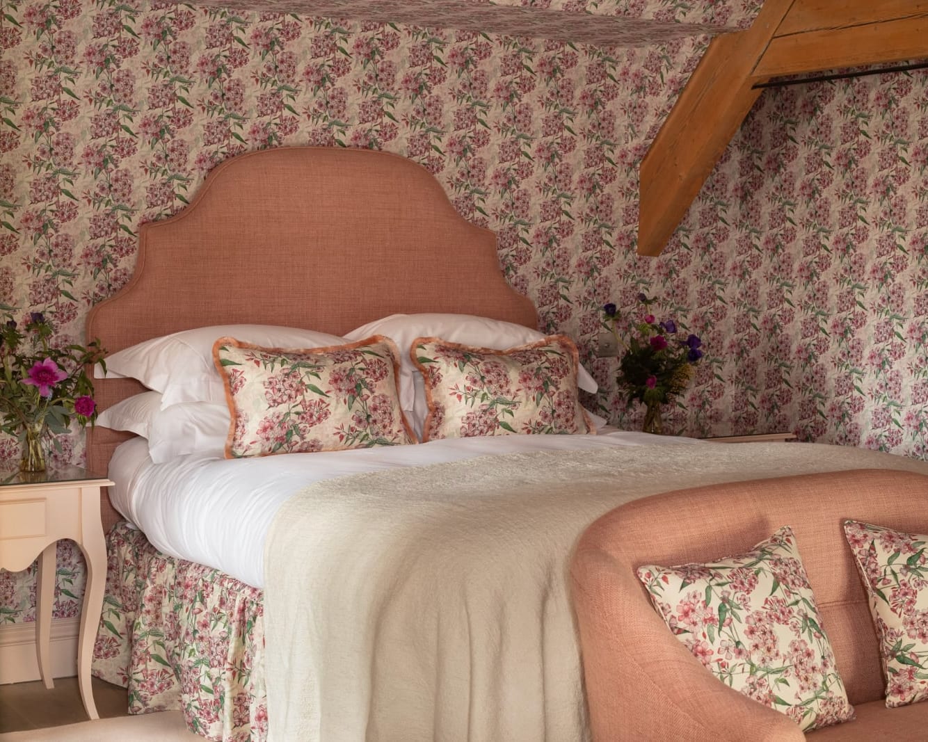 pink headboard on a white bed with floral patterned wall paper behind