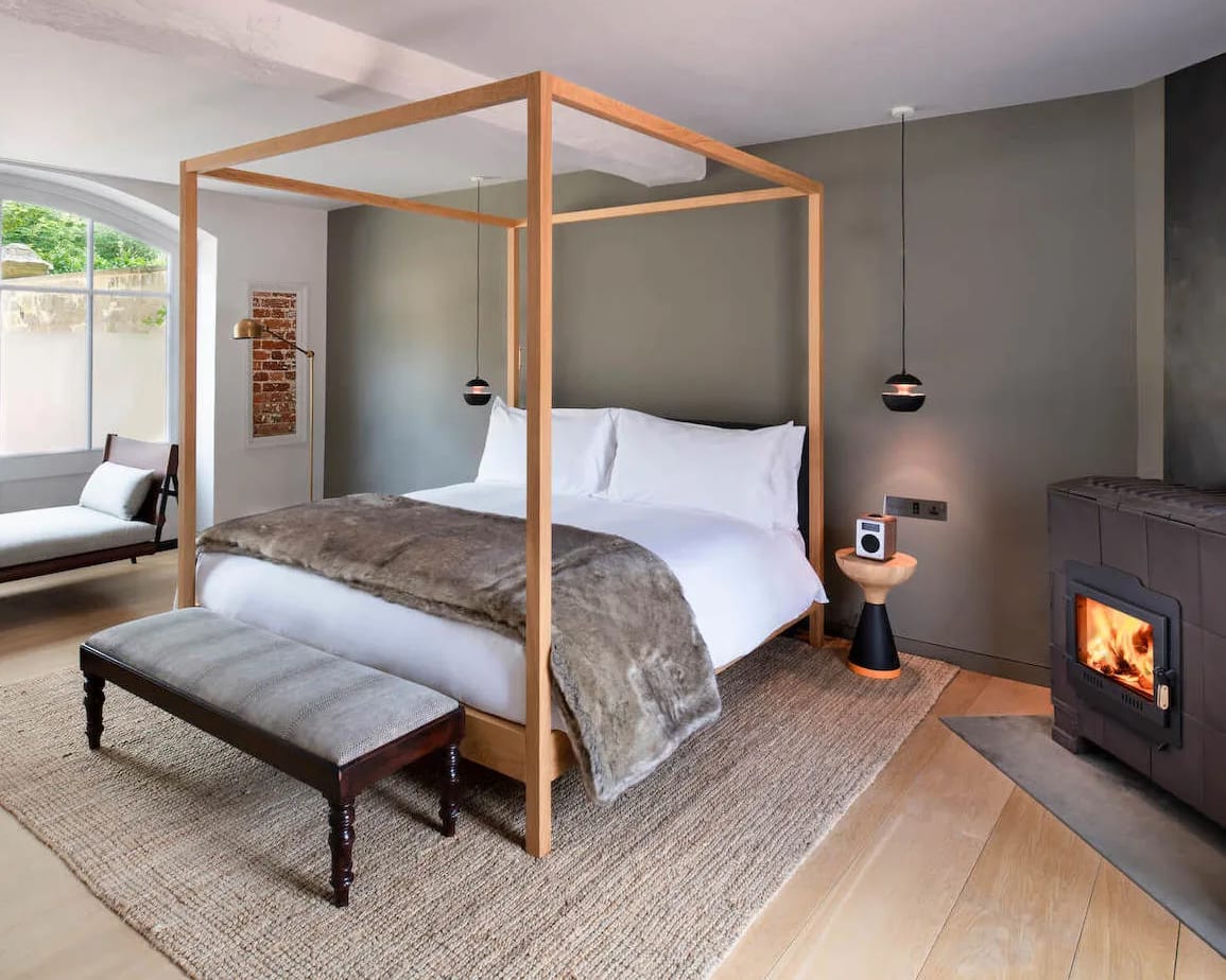 modern hotel room with four poster bed, faux fur blanket, fireplace, and grey walls