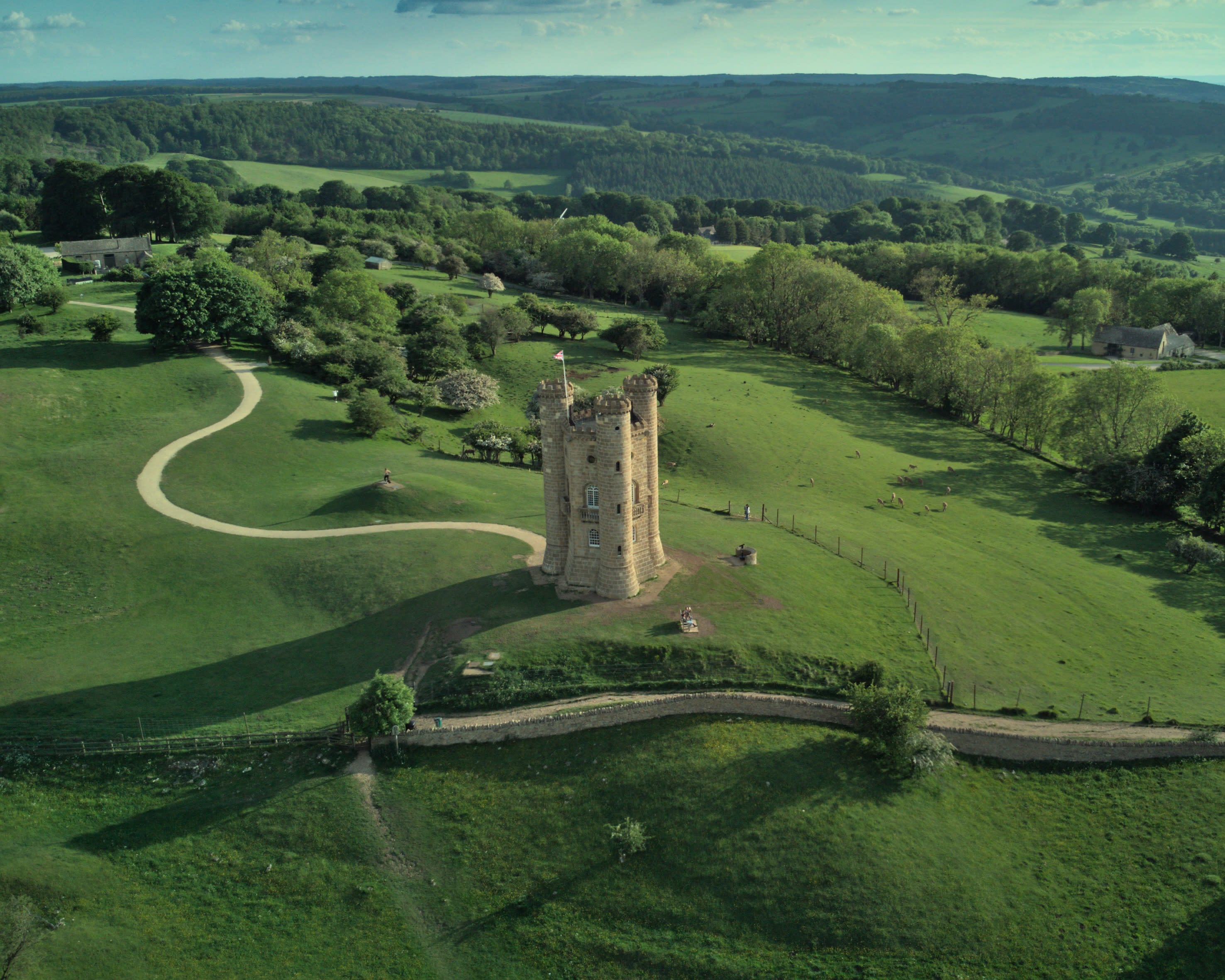 aerial of tall castle tower on rolling green hills with forested hills in the background