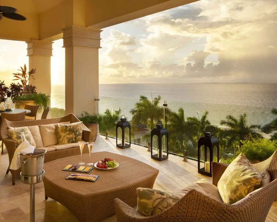 Terrace with rattan outdoor furniture overlooking palm trees and ocean at sunset
