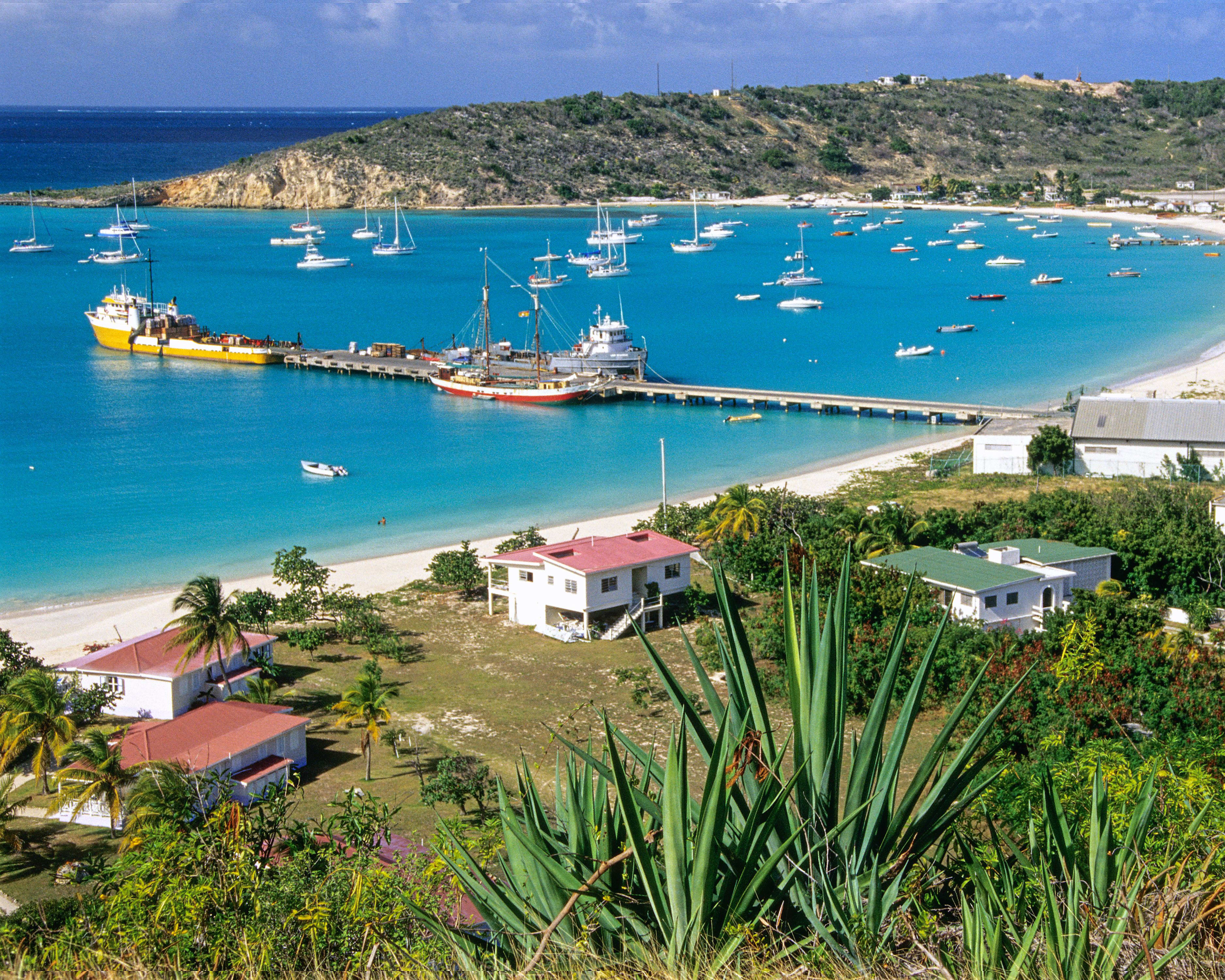 a historic small coastal Caribbean town with pier and small boats in turquoise harbor and green shrubs