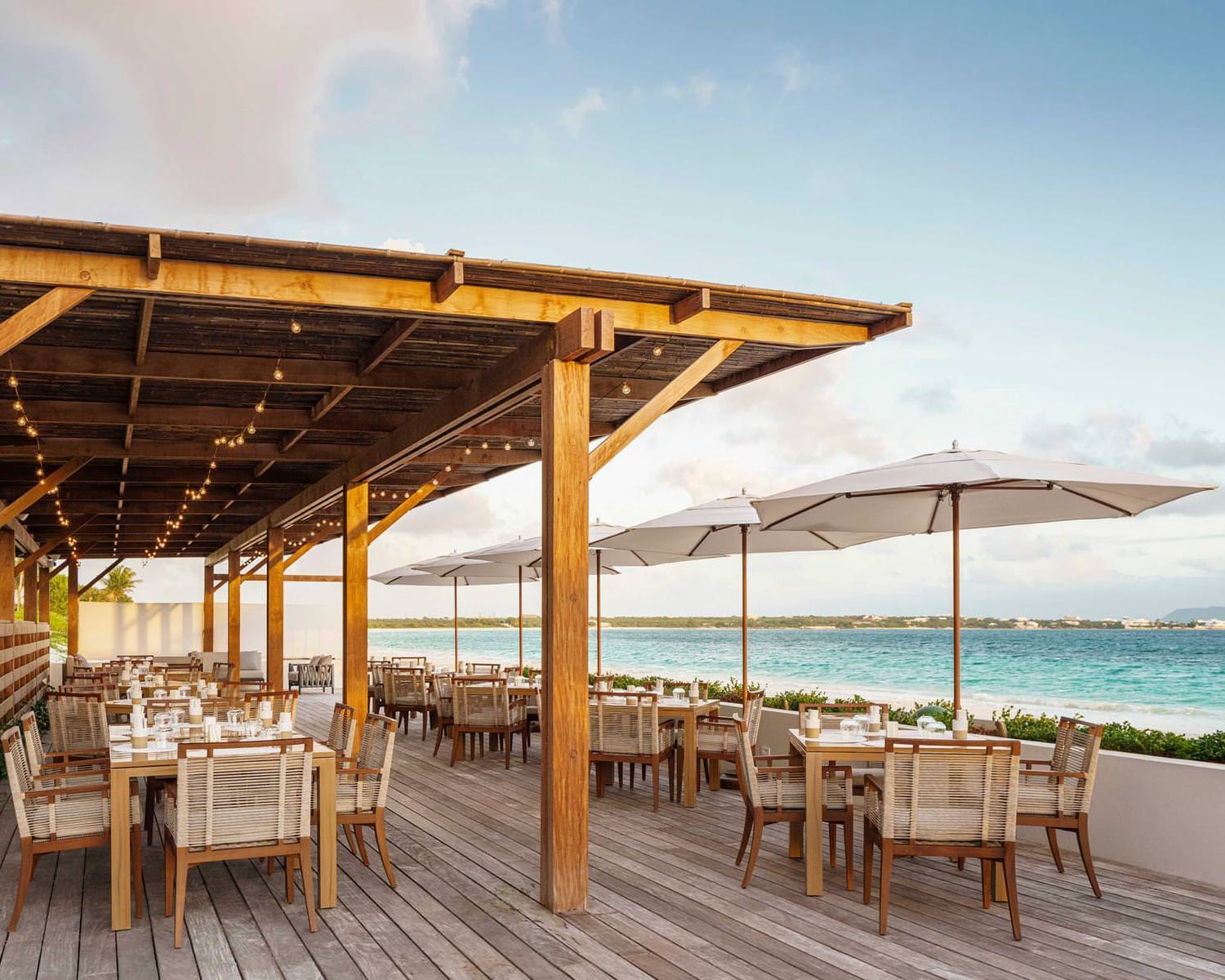 beachfront restaurant cafe with umbrellas and pergola with lights over tables and chairs on an outdoor beachfront terrace