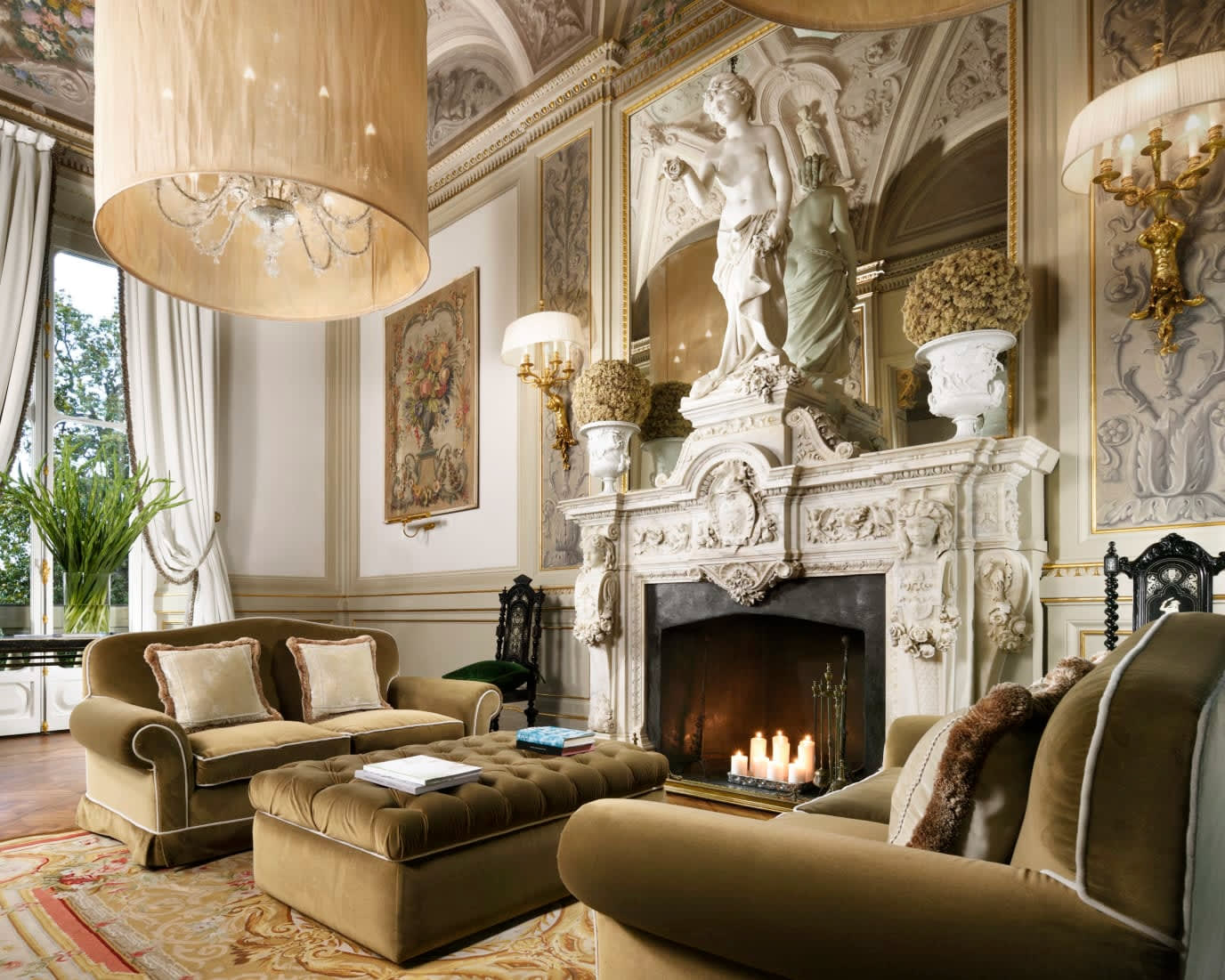 luxurious velvet olive sofas in front of an ornate white fireplace under a chandelier