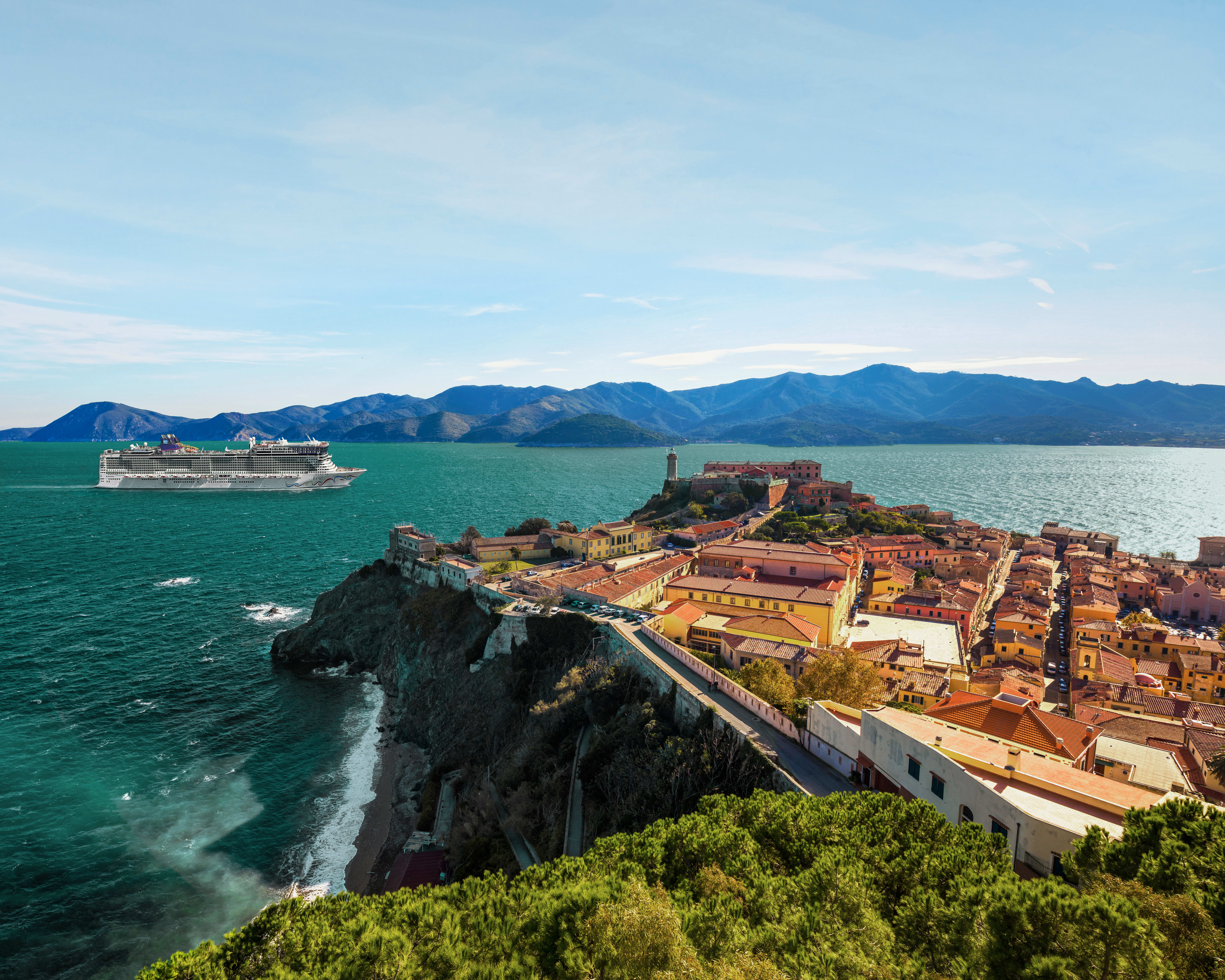 a clifftop red roofed town on the turquoise ocean with a cruise ship offshore