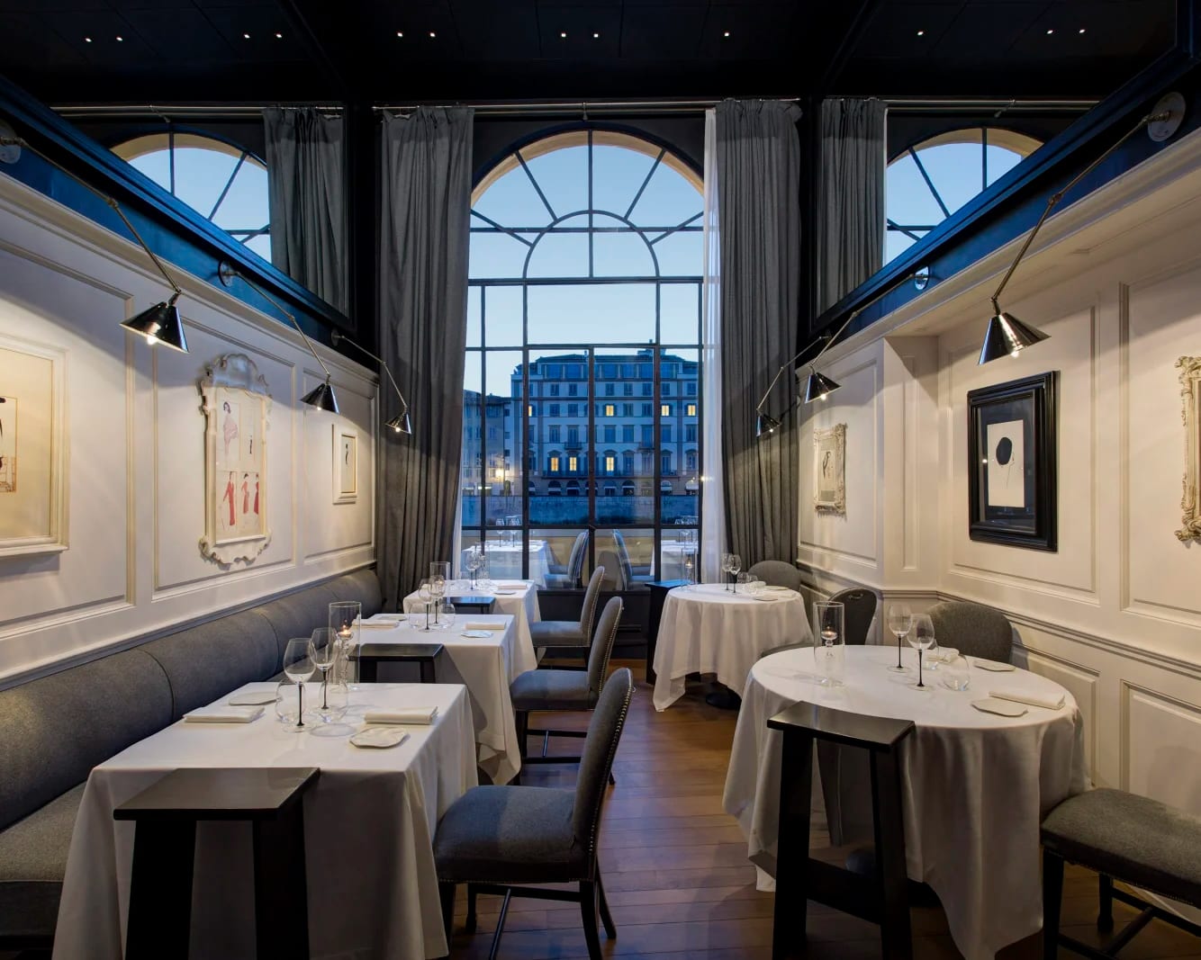 a dimly lit modern restaurants with white table cloths, gray chairs, and white walls with lit artwork