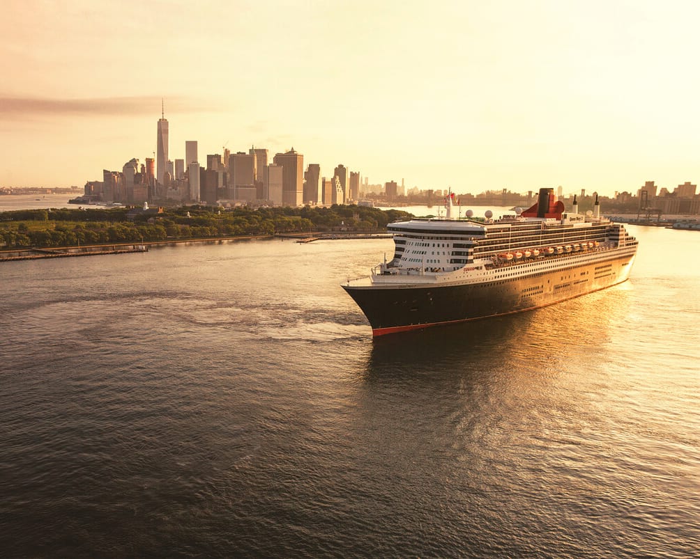 white, black and red ocean liner leaving port with the sun setting and city skyline in background