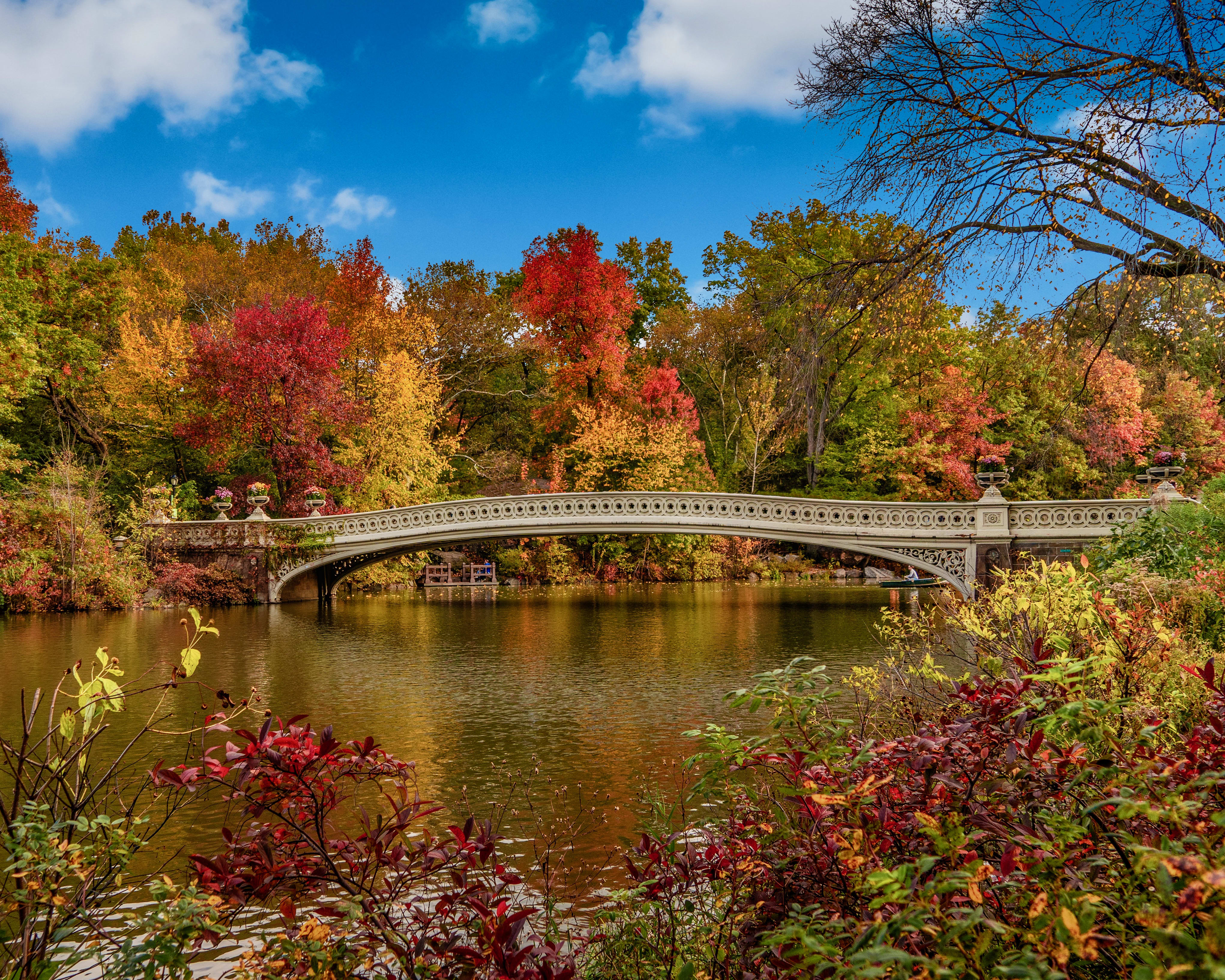 a stone bridge over a lake with autumn colored trees around the water during day