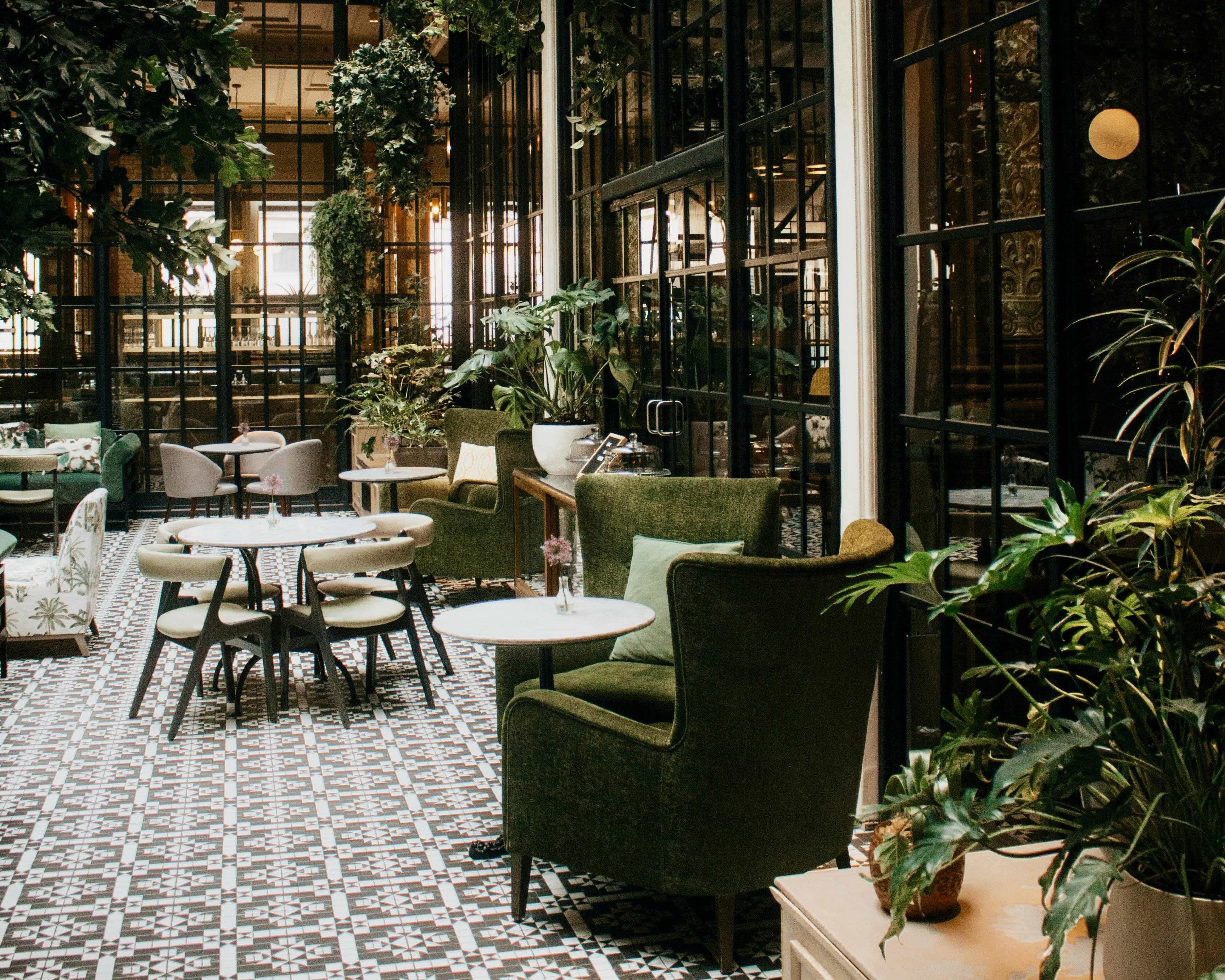 modern black metal and glass restaurant space with white tables, wood chairs, and green fabric loungers and plants