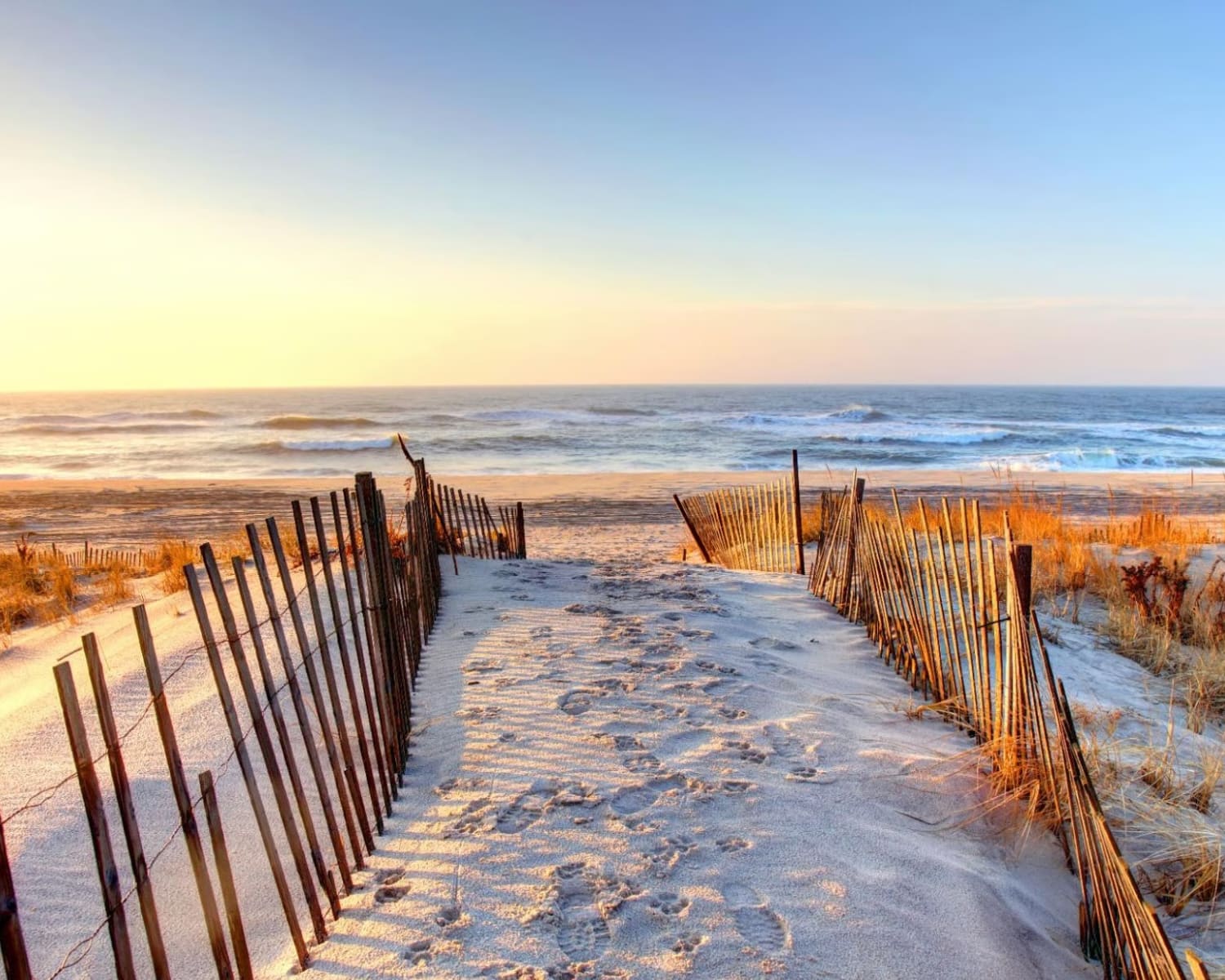 white sand footpath lined with rustic wood pilings and an ocean in front