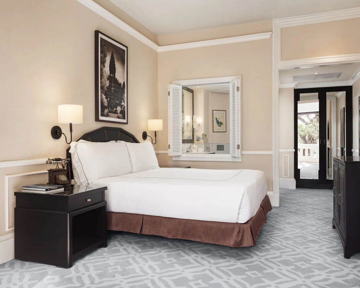 Brown framed hotel bed with white sheets and cream walls