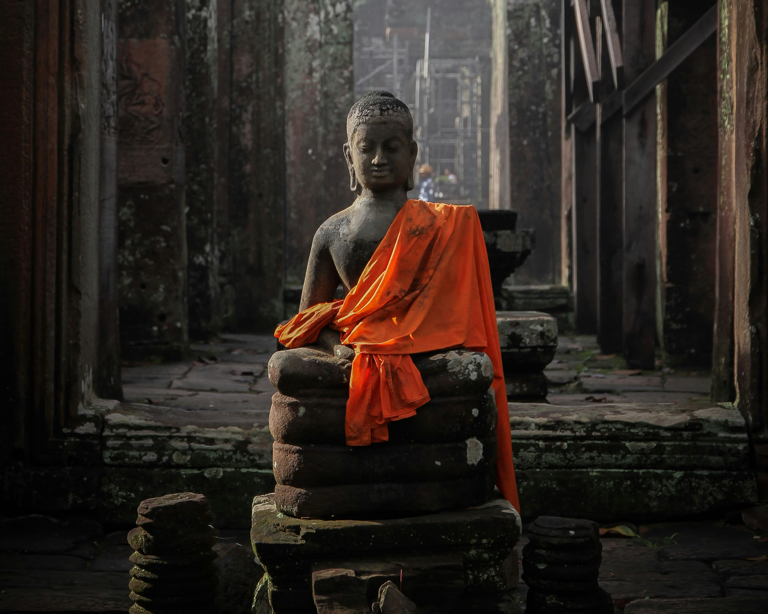 a dark stone buddha statue draped in orange robe during day