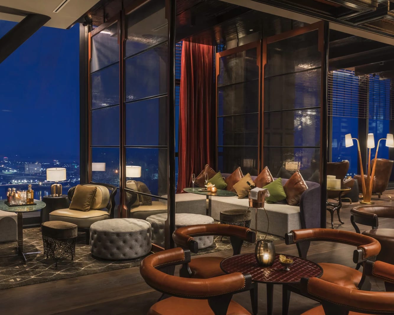 a modern lounge with earth colored chairs and floor to ceiling windows overlooking a city at night