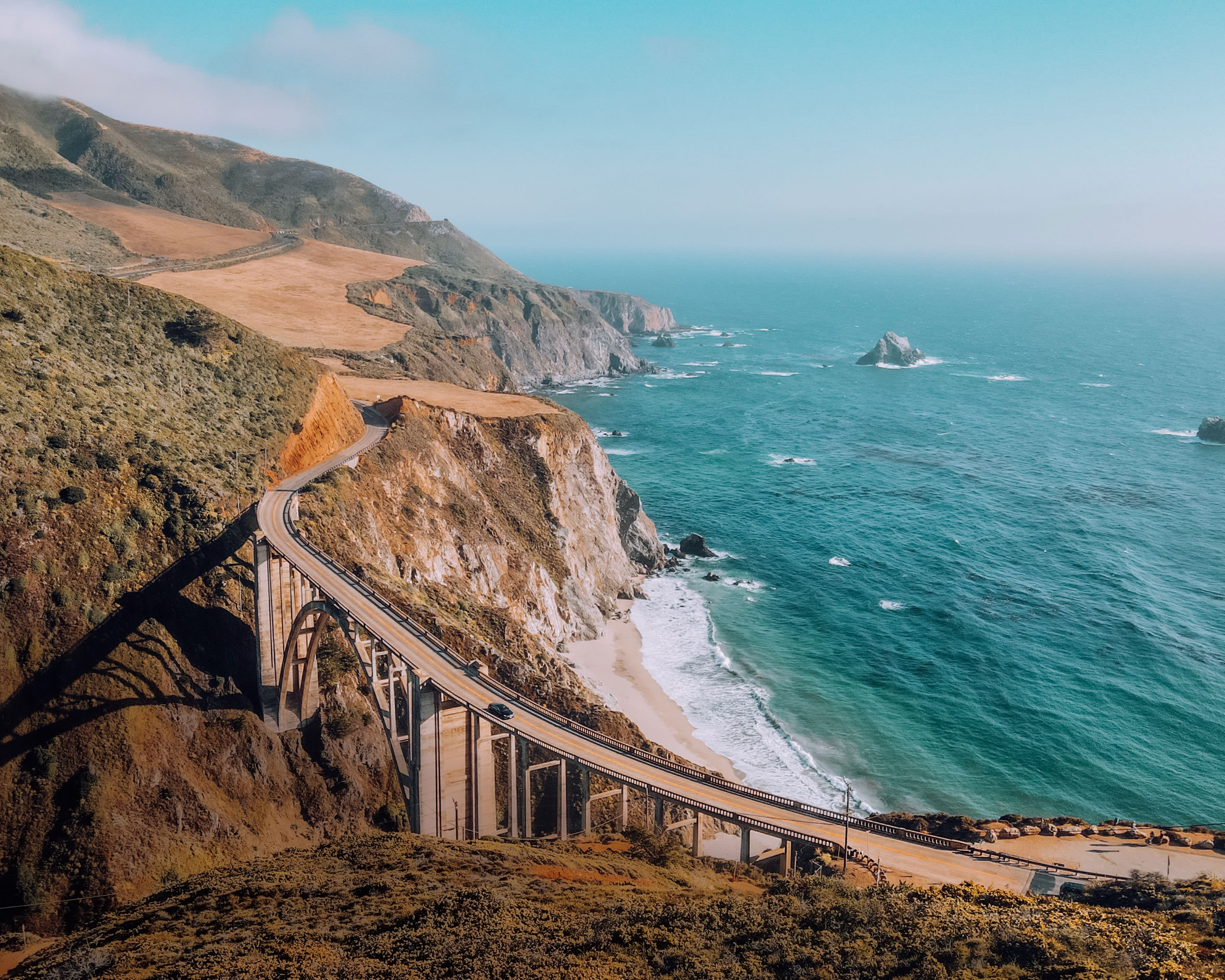 clifftop bridge over a canyon along the ocean during day