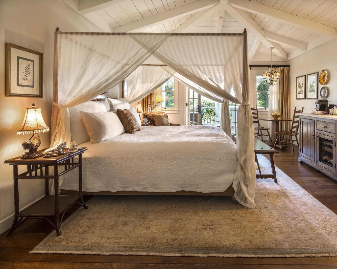 white curtained four poster bed under vaulted white wood ceilings in a cozy cottage