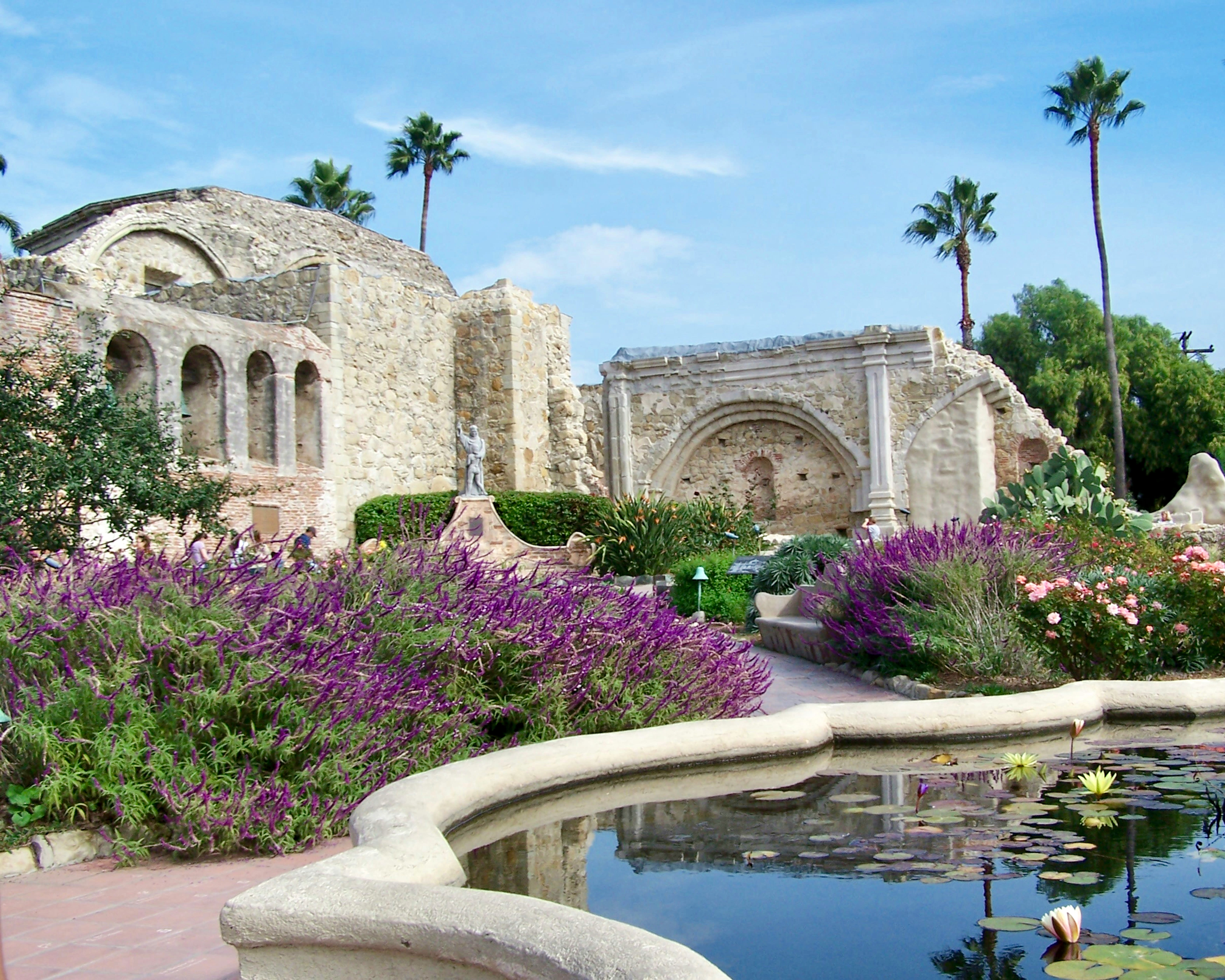 white stone ruins with lavender plants, water fountain, and palm trees