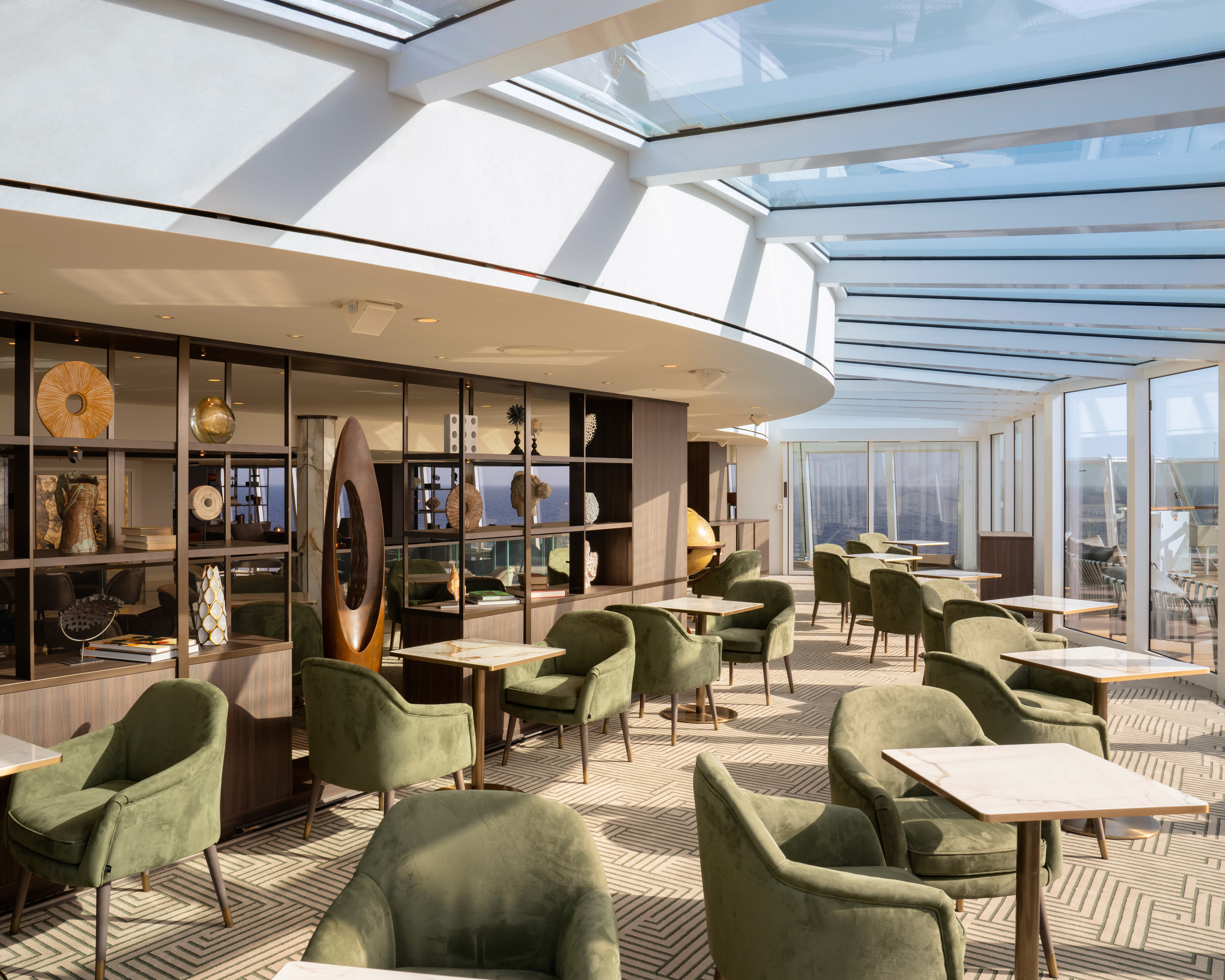 cruise ship lounge with glass ceiling, green velvet chairs, and dark wood book shelves