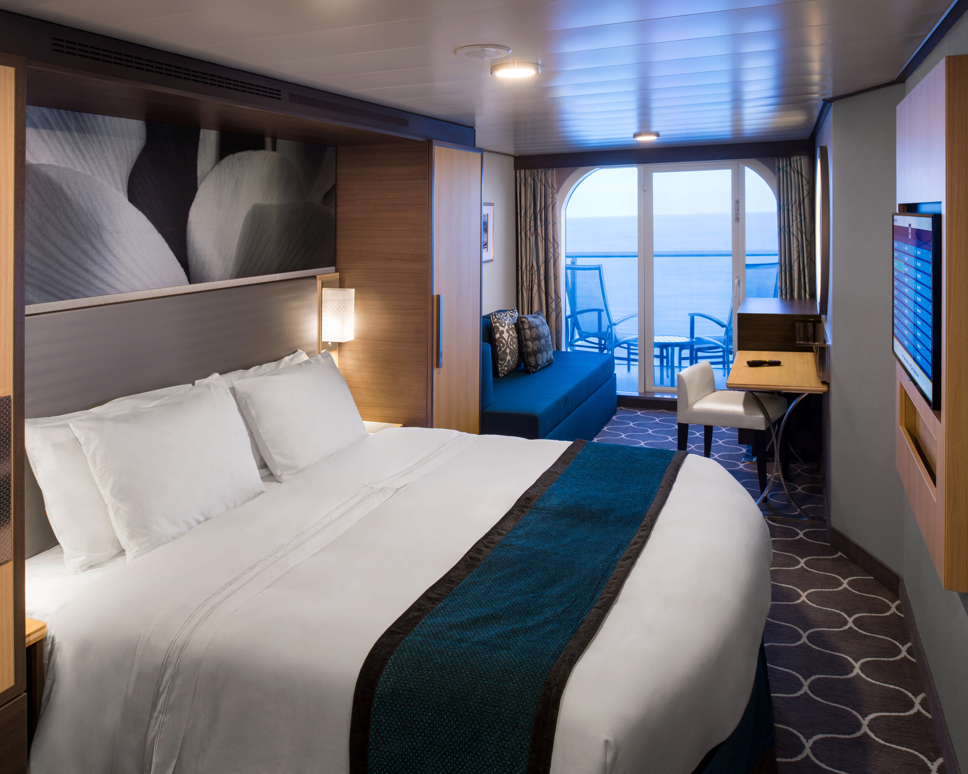 balcony cruise cabin with white bed sheets, teal blanket and sofa, and brown carpet