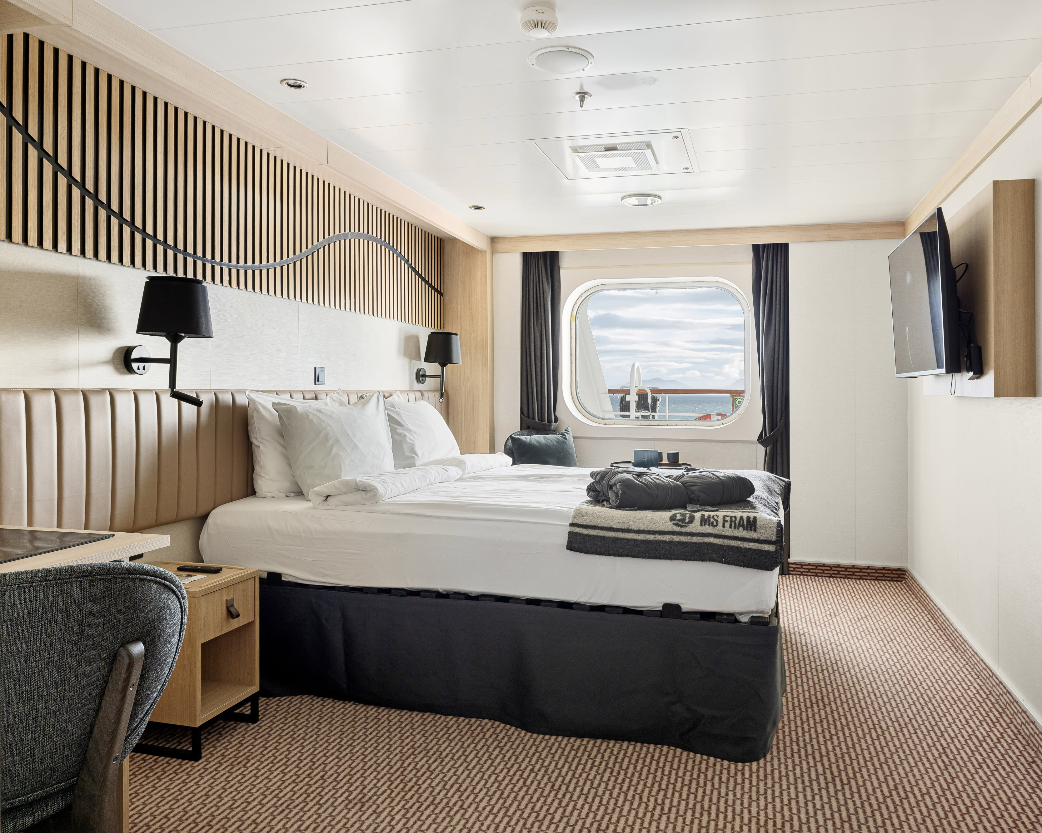 expedition cruise cabin with dark grey fabrics, white sheets, and light tan wood