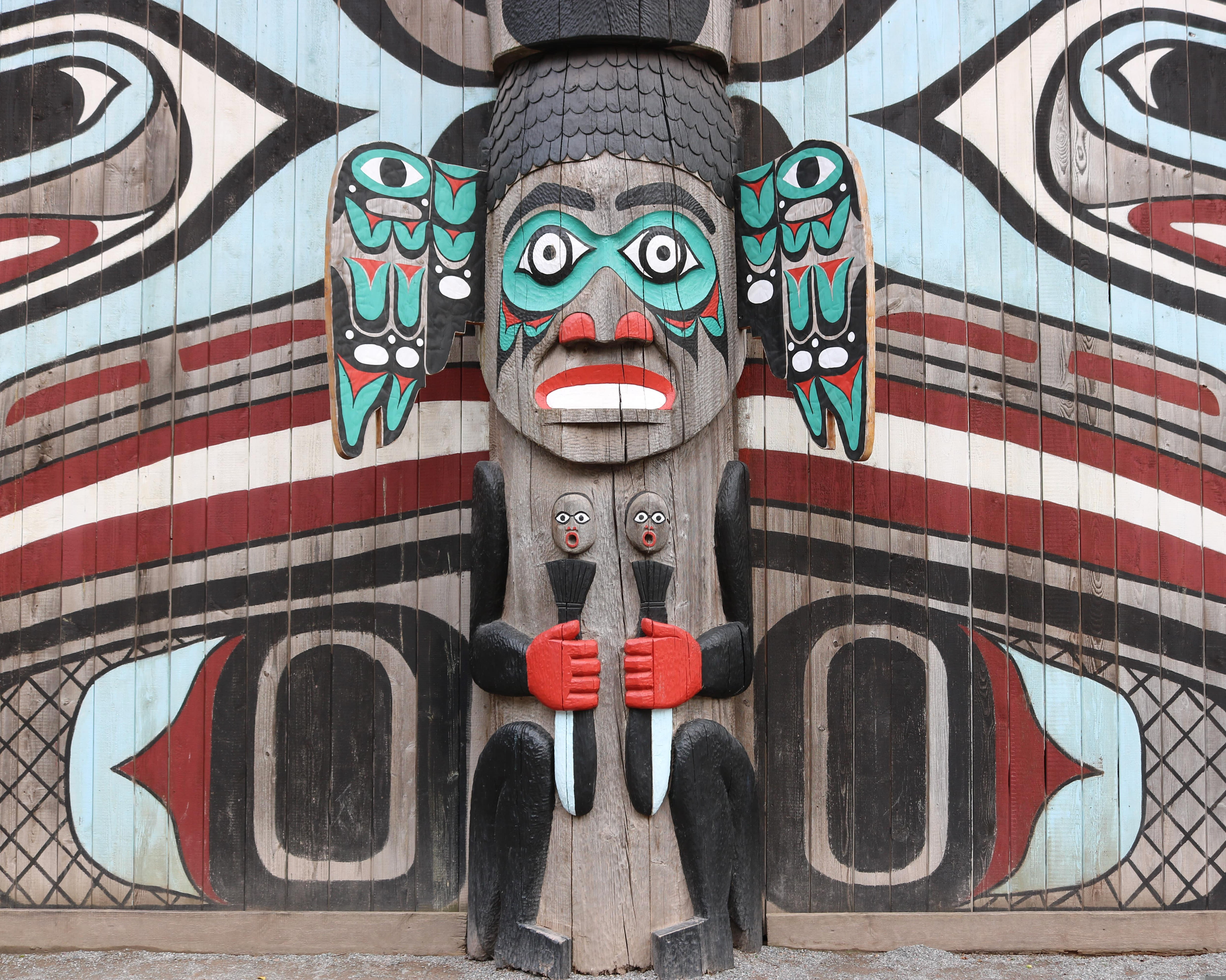 wood carved totem pole with black, white, red, and bright aqua paint