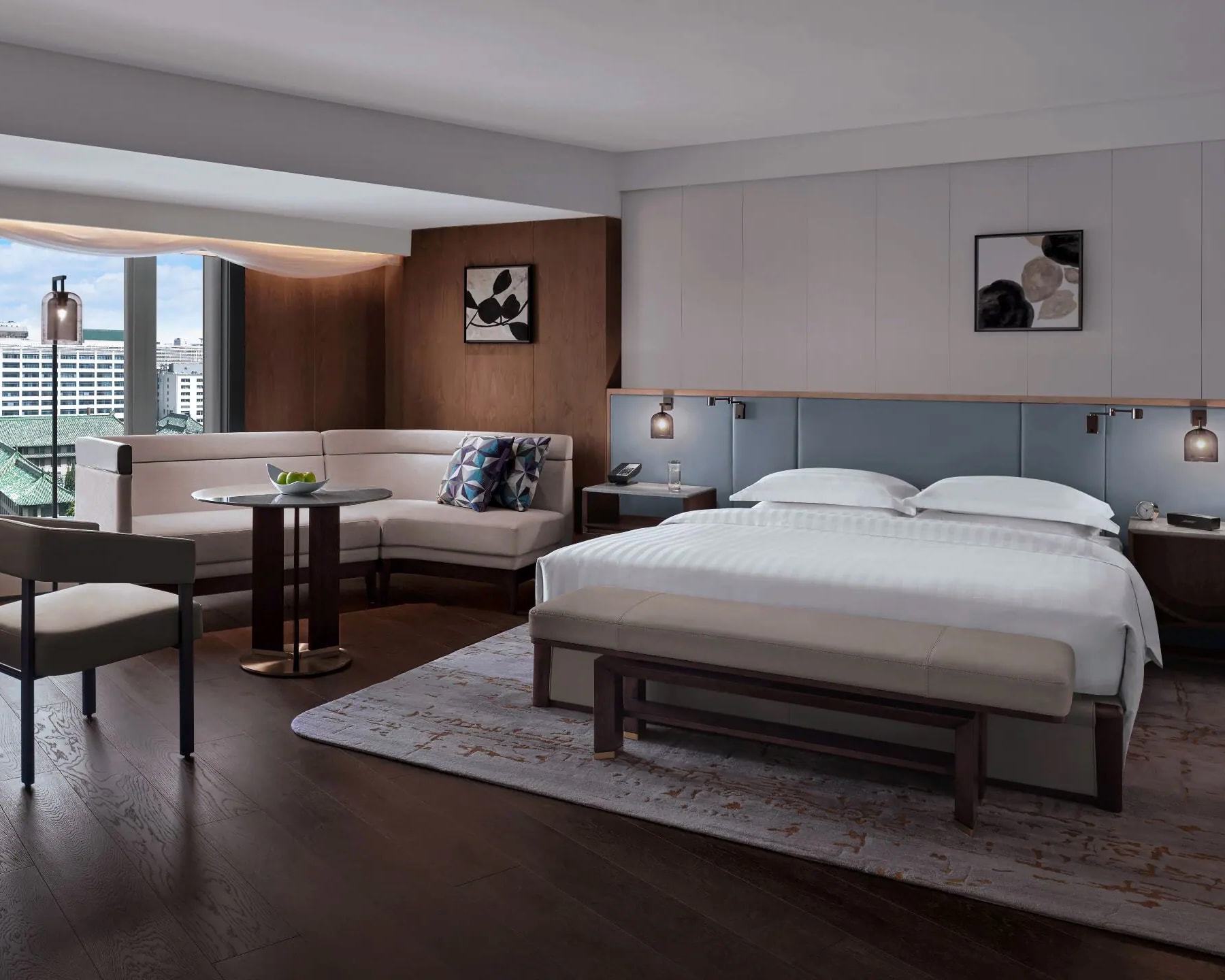 modern hotel room with white bed, light blue headboard, and tan sofa next to a window and warm woods