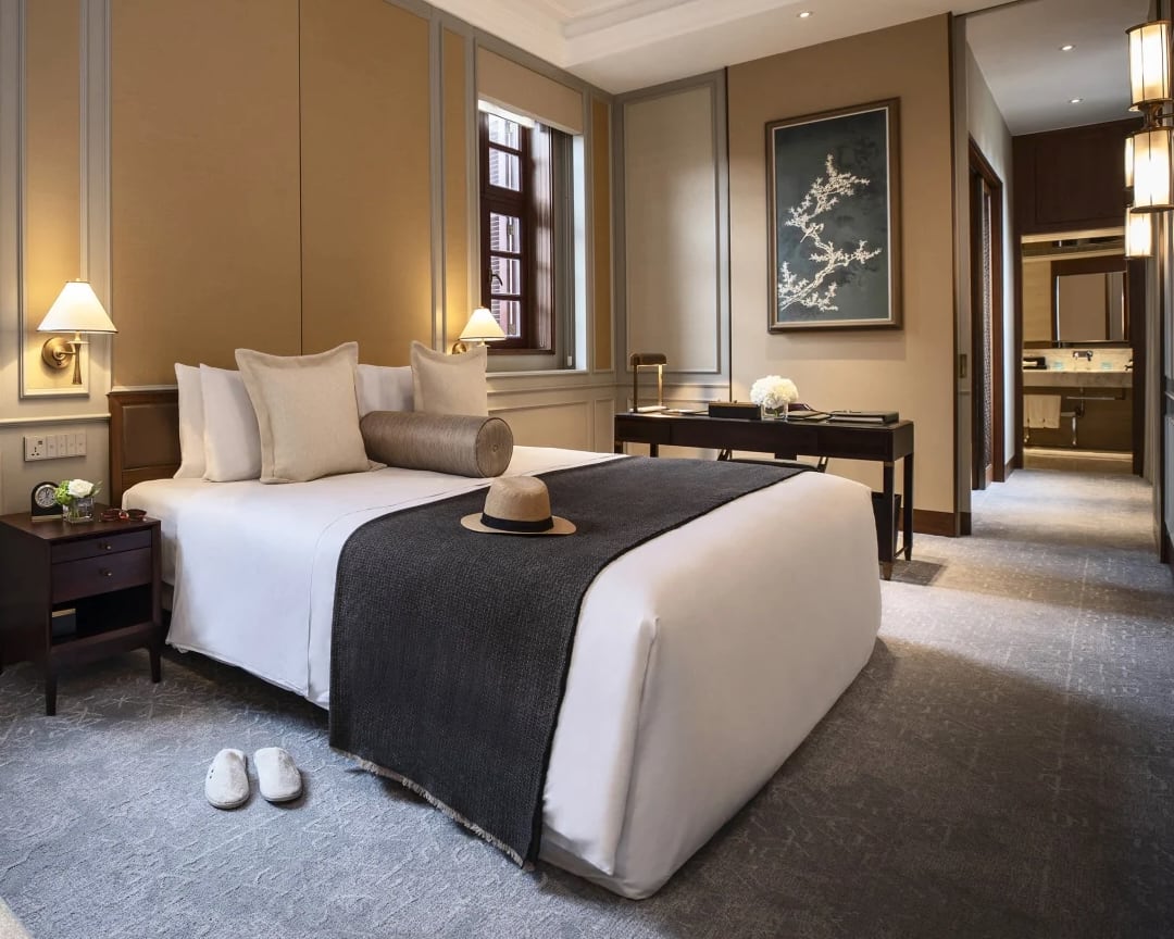 hotel room with white bed, grey blanket, dark wood furniture, and cream walls