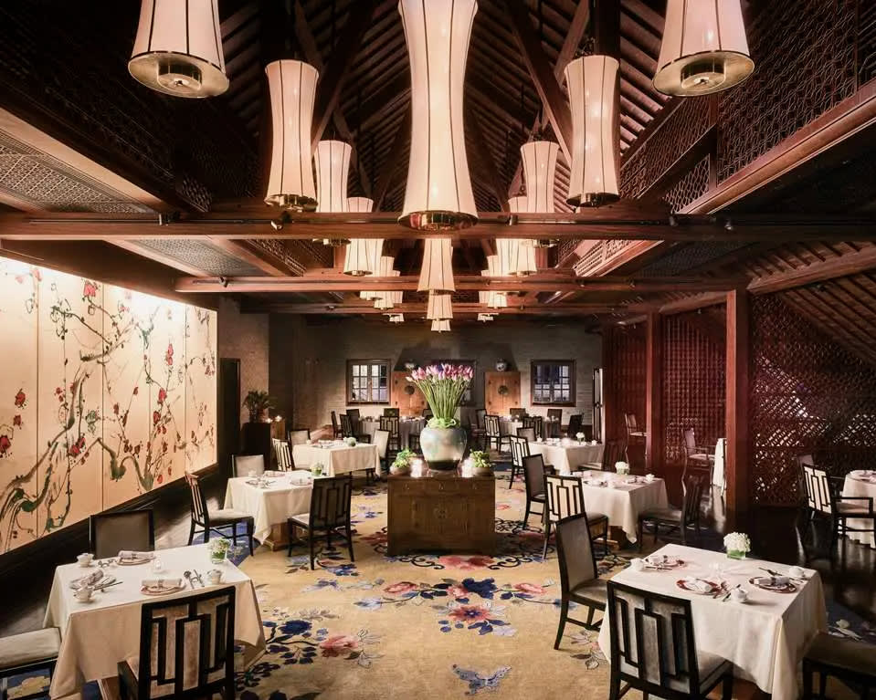 elegant fine dining with floral carpets and walls, ornate black chairs, white table linens, and wood beams with soft lights